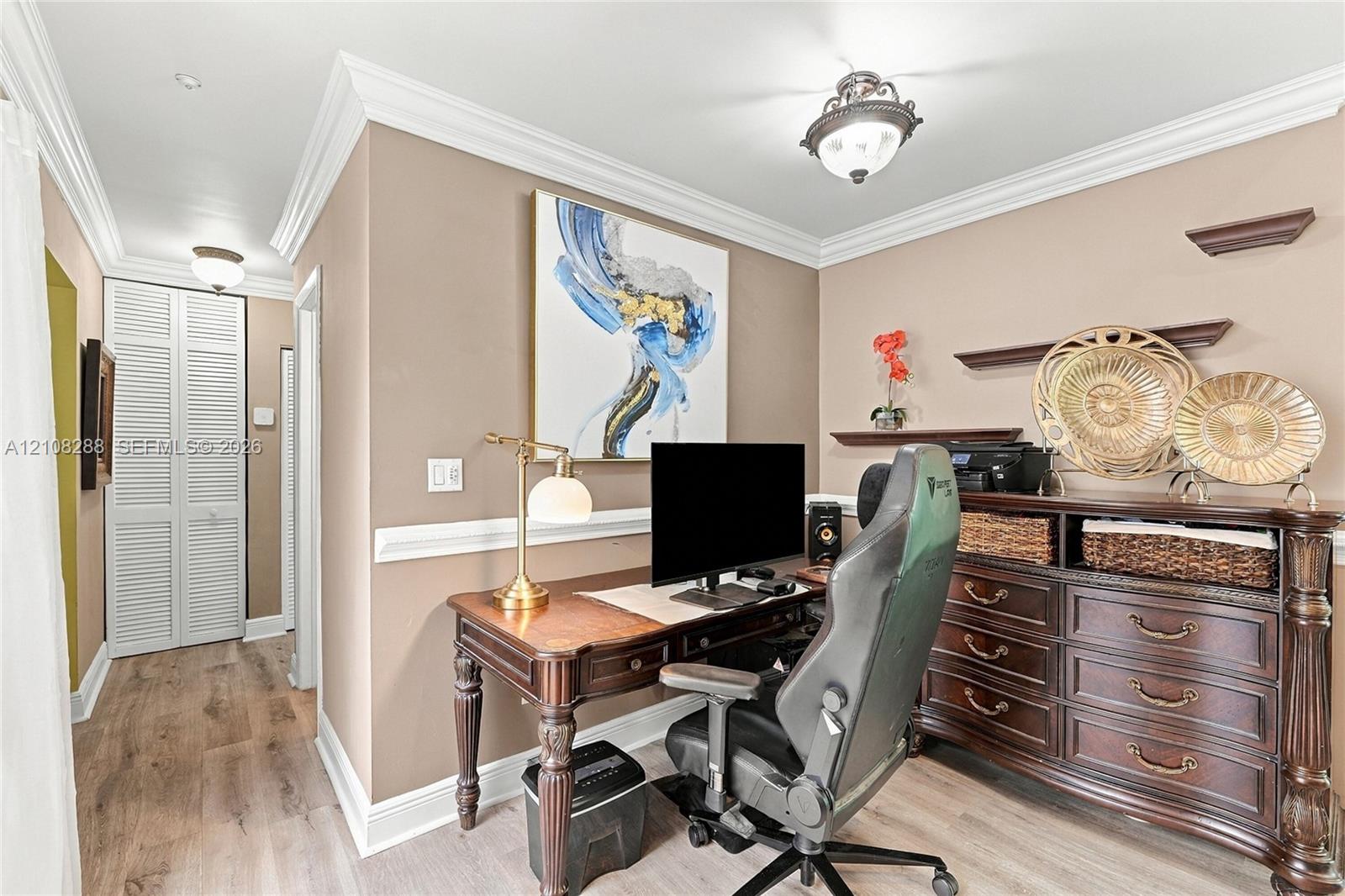 Room featuring wood-finish flooring, crown molding, chair rail trim, louvered bi-fold closet doors, and a semi-flush mount ceiling fixture Room featuring wood-finish flooring, crown molding, chair rail trim, louvered bi-fold closet doors, and a semi-flush mount ceiling fixture
