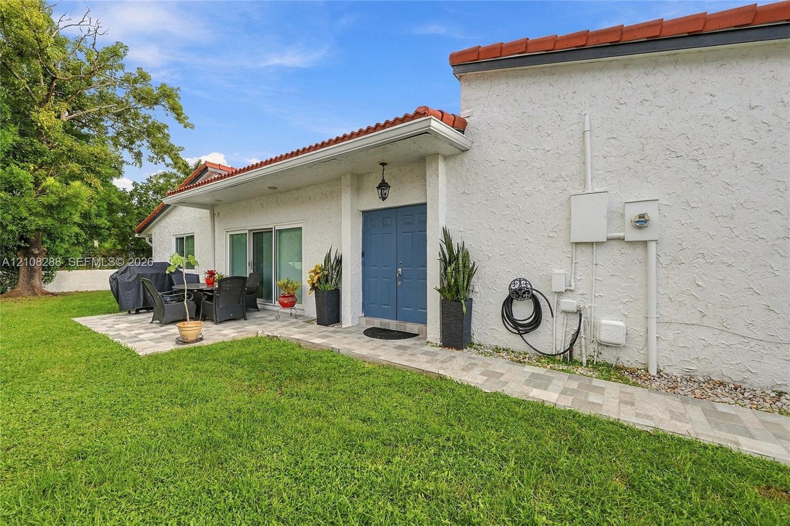 Stucco exterior featuring a dual-tone tile roof, blue double entry doors, and expansive paver patio hardscaping Stucco exterior featuring a dual-tone tile roof, blue double entry doors, and expansive paver patio hardscaping