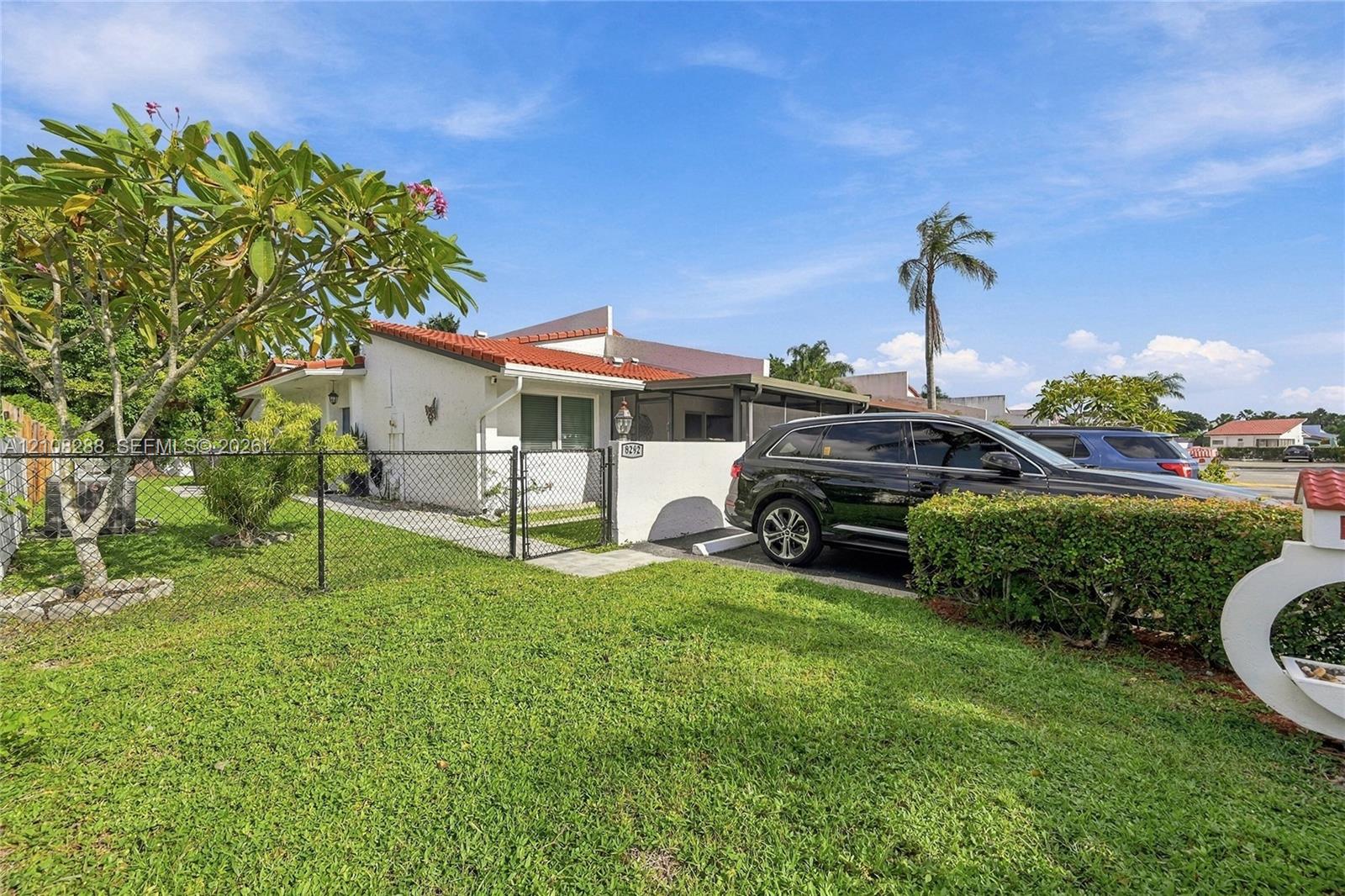 Stucco exterior featuring a terracotta-tiled roof, covered parking structure, fenced front yard, and landscaped grounds Stucco exterior featuring a terracotta-tiled roof, covered parking structure, fenced front yard, and landscaped grounds