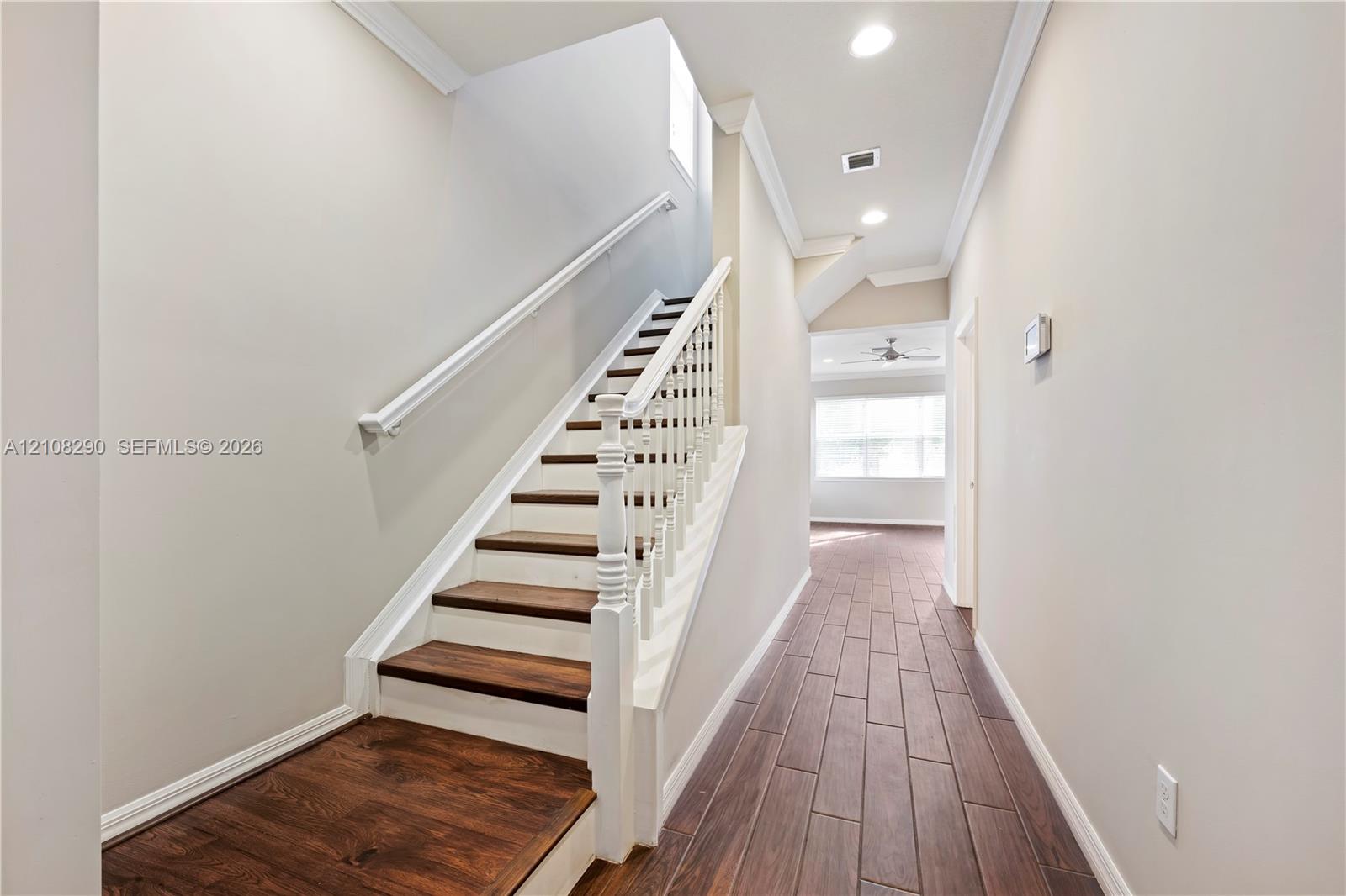 Interior hallway featuring wood-finish flooring, staircase with white spindle railings, wood-toned treads, and recessed lighting Interior hallway featuring wood-finish flooring, staircase with white spindle railings, wood-toned treads, and recessed lighting