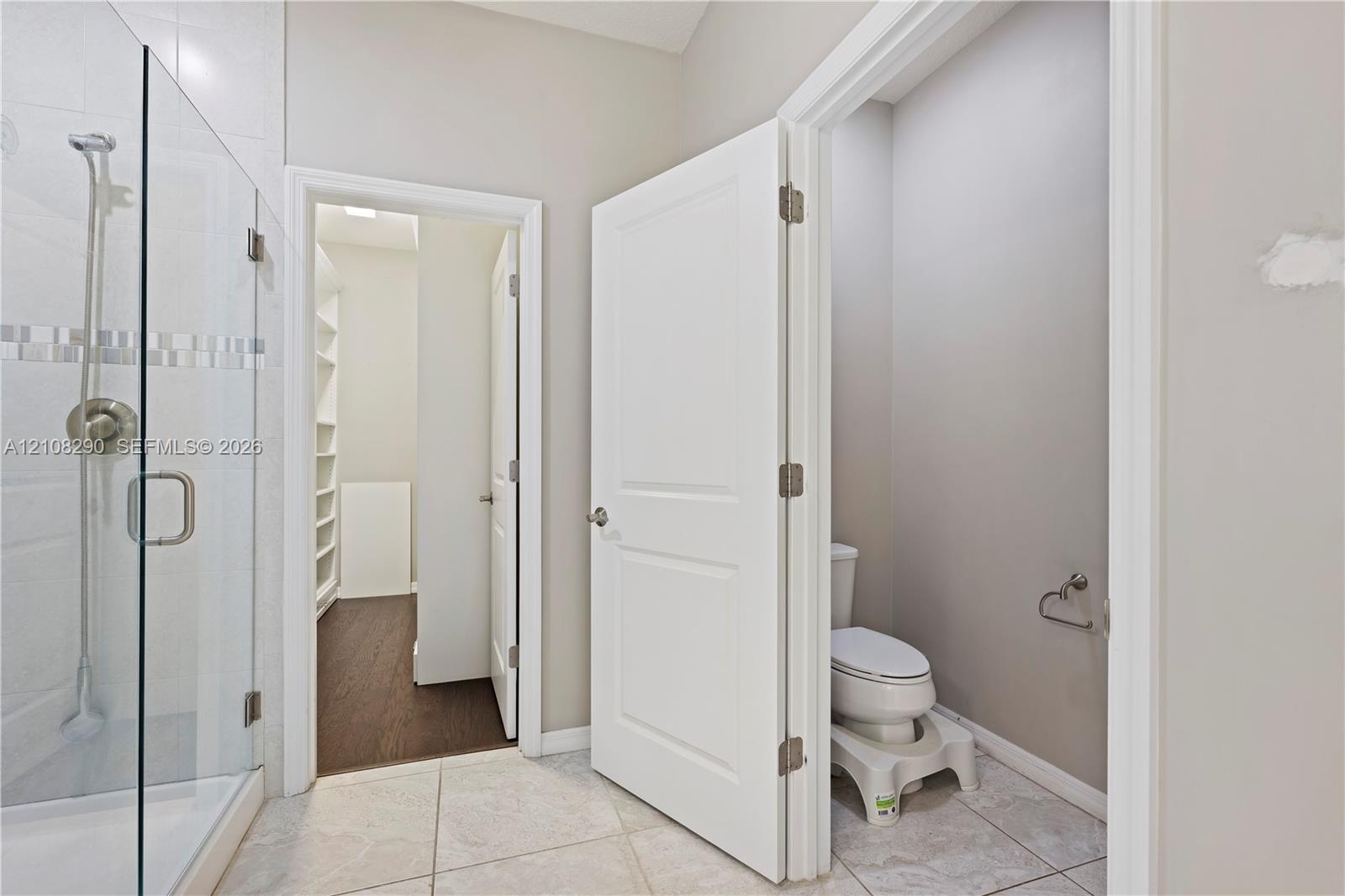 Walk-in shower with a glass enclosure, tile flooring, and a separate water closet featuring a two-panel door