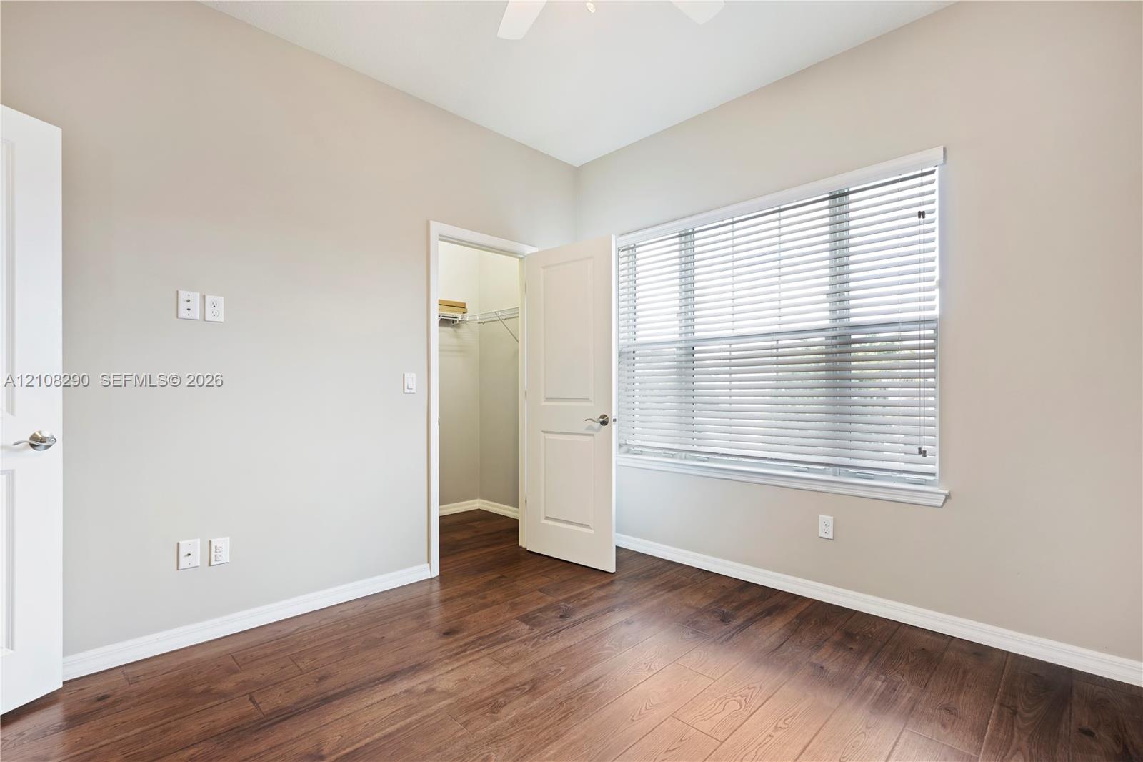 Interior space featuring wood-finish flooring, a neutral wall palette, a walk-in closet, and a window with horizontal blinds