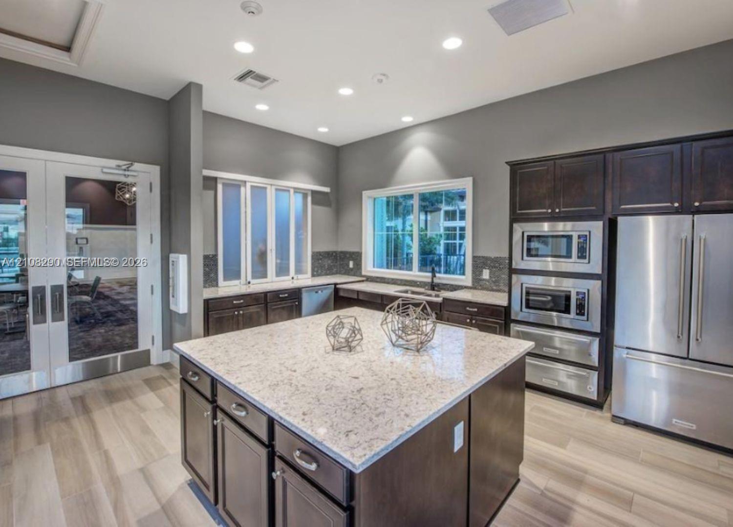 Kitchen featuring a central island with a stone countertop, dark wood cabinetry, stainless steel built-in appliances, recessed lighting, and wood-finish flooring