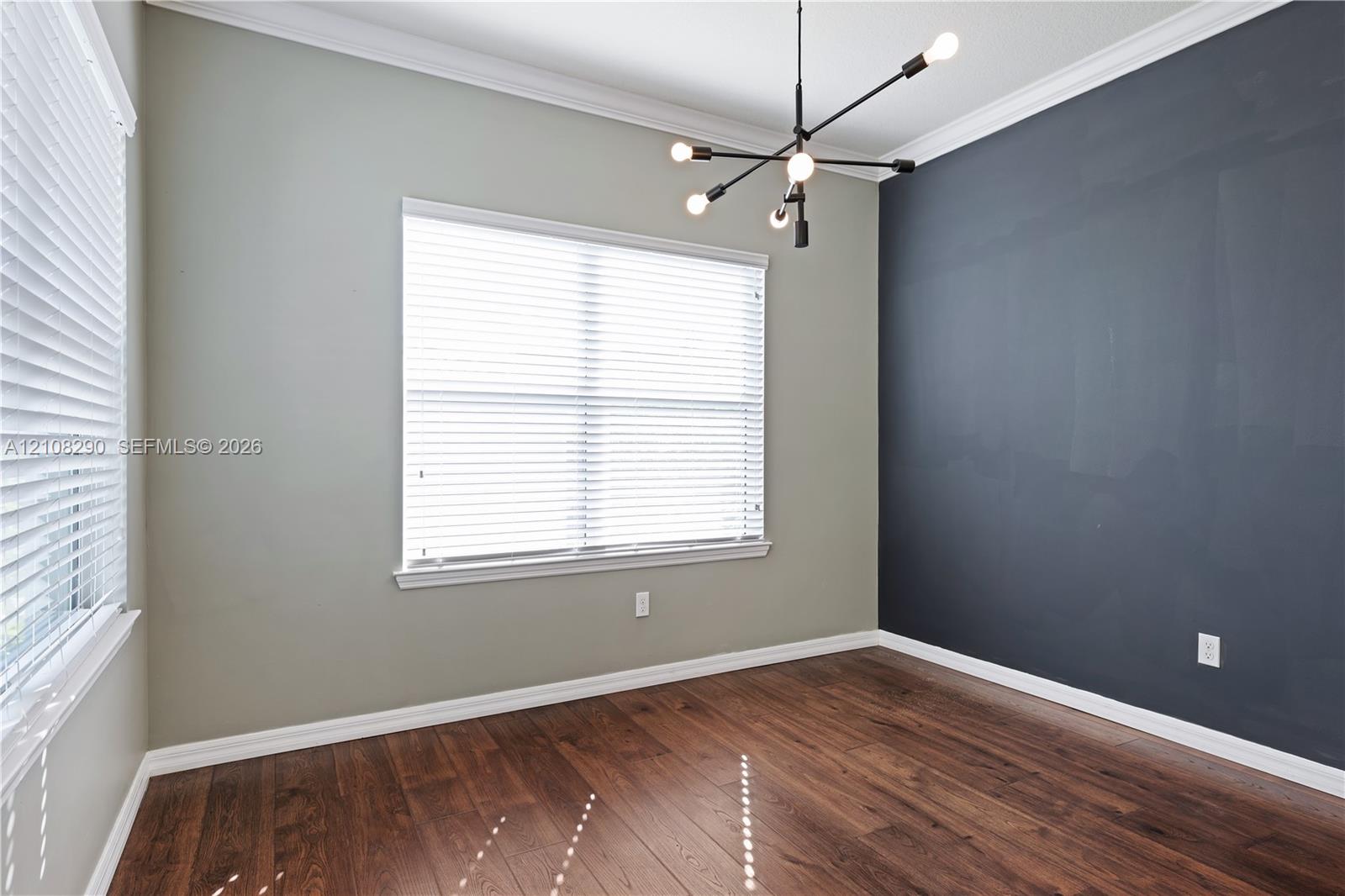 Room featuring wood-finish flooring, a dark accent wall, crown molding, and a contemporary multi-arm chandelier