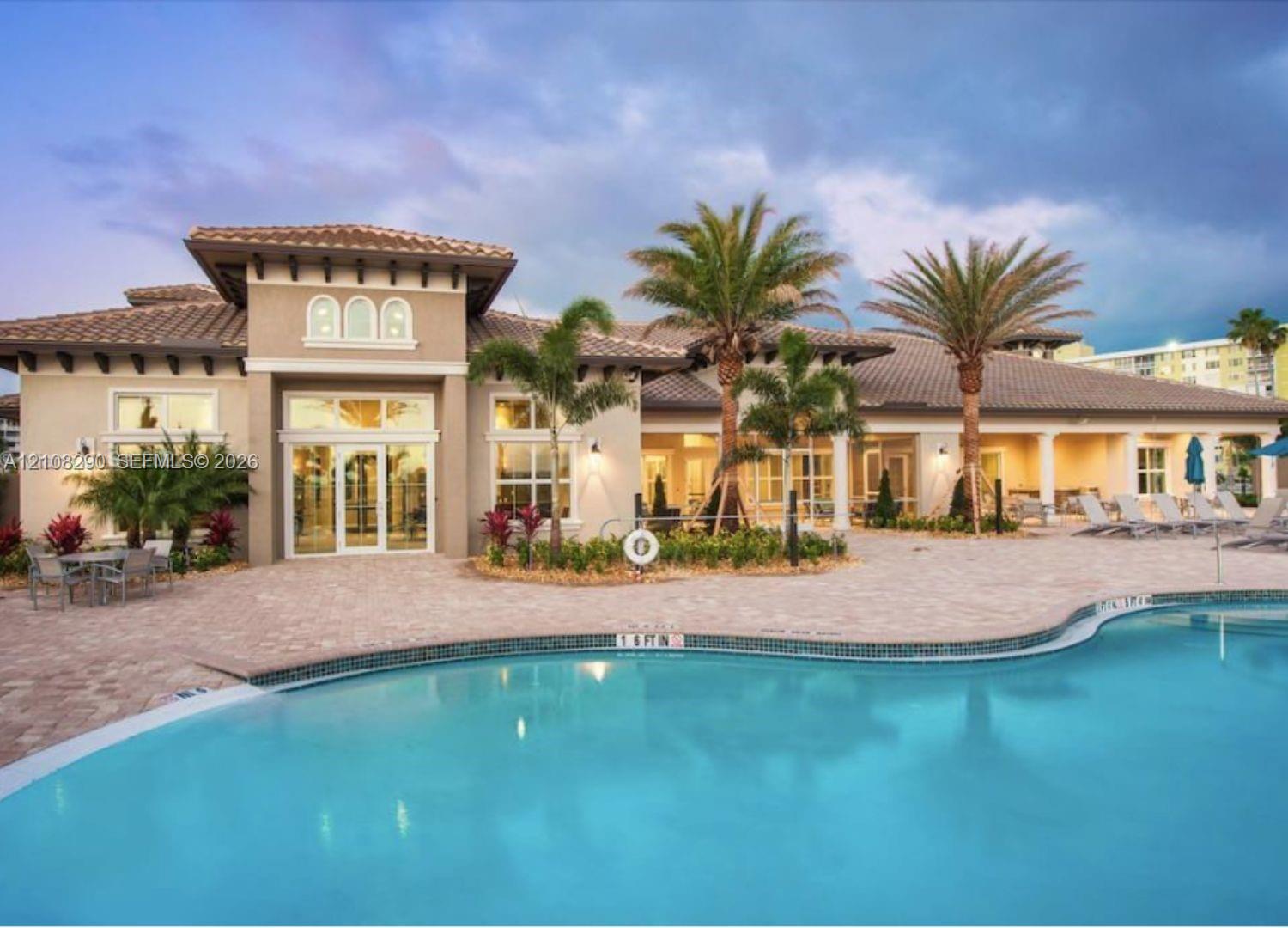 Stucco exterior featuring a multi-tiered tile roof, covered patio area, brick-paver pool deck, and freeform swimming pool with integrated landscaping