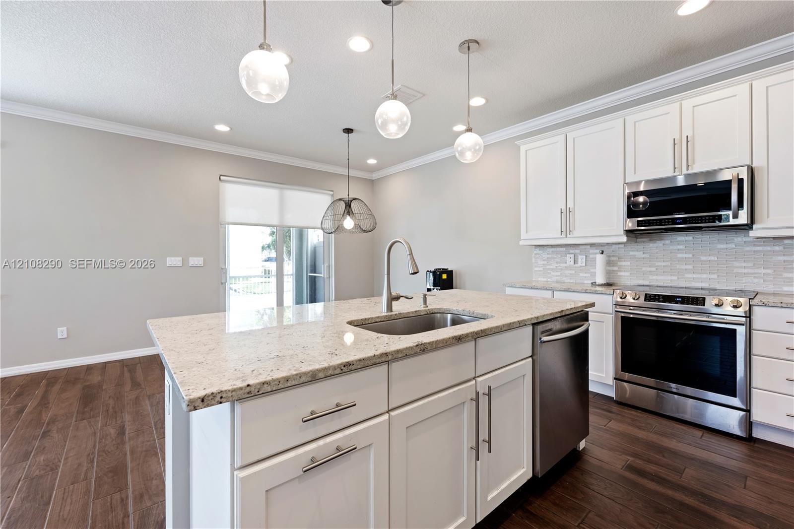 Kitchen featuring white shaker-style cabinetry, stone countertops, stainless steel appliances, wood-finish flooring, and multi-pendant lighting Kitchen featuring white shaker-style cabinetry, stone countertops, stainless steel appliances, wood-finish flooring, and multi-pendant lighting