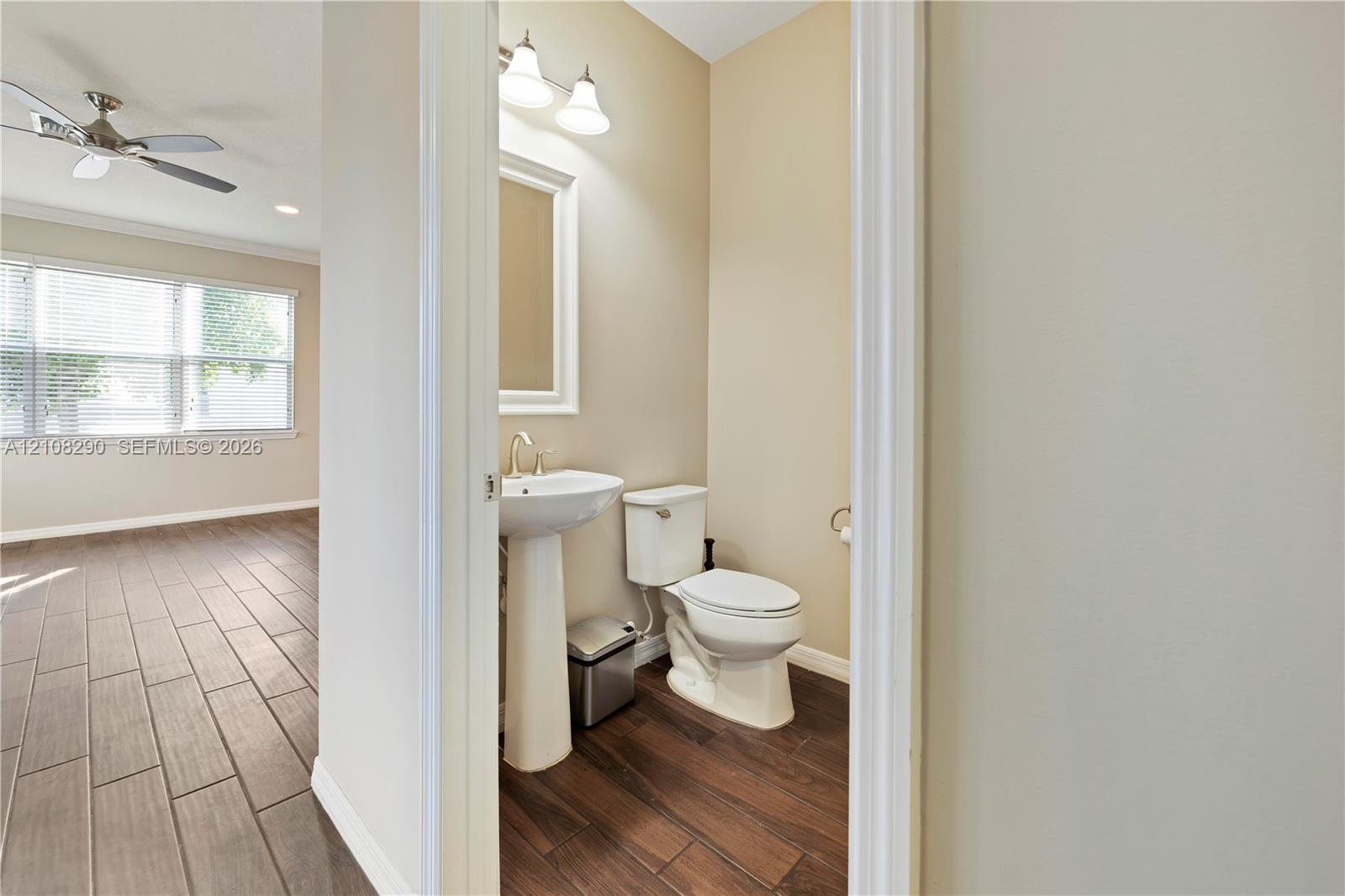 Pedestal sink with a polished metal faucet, multi-light fixture, white toilet, and wood-finish tile flooring Pedestal sink with a polished metal faucet, multi-light fixture, white toilet, and wood-finish tile flooring