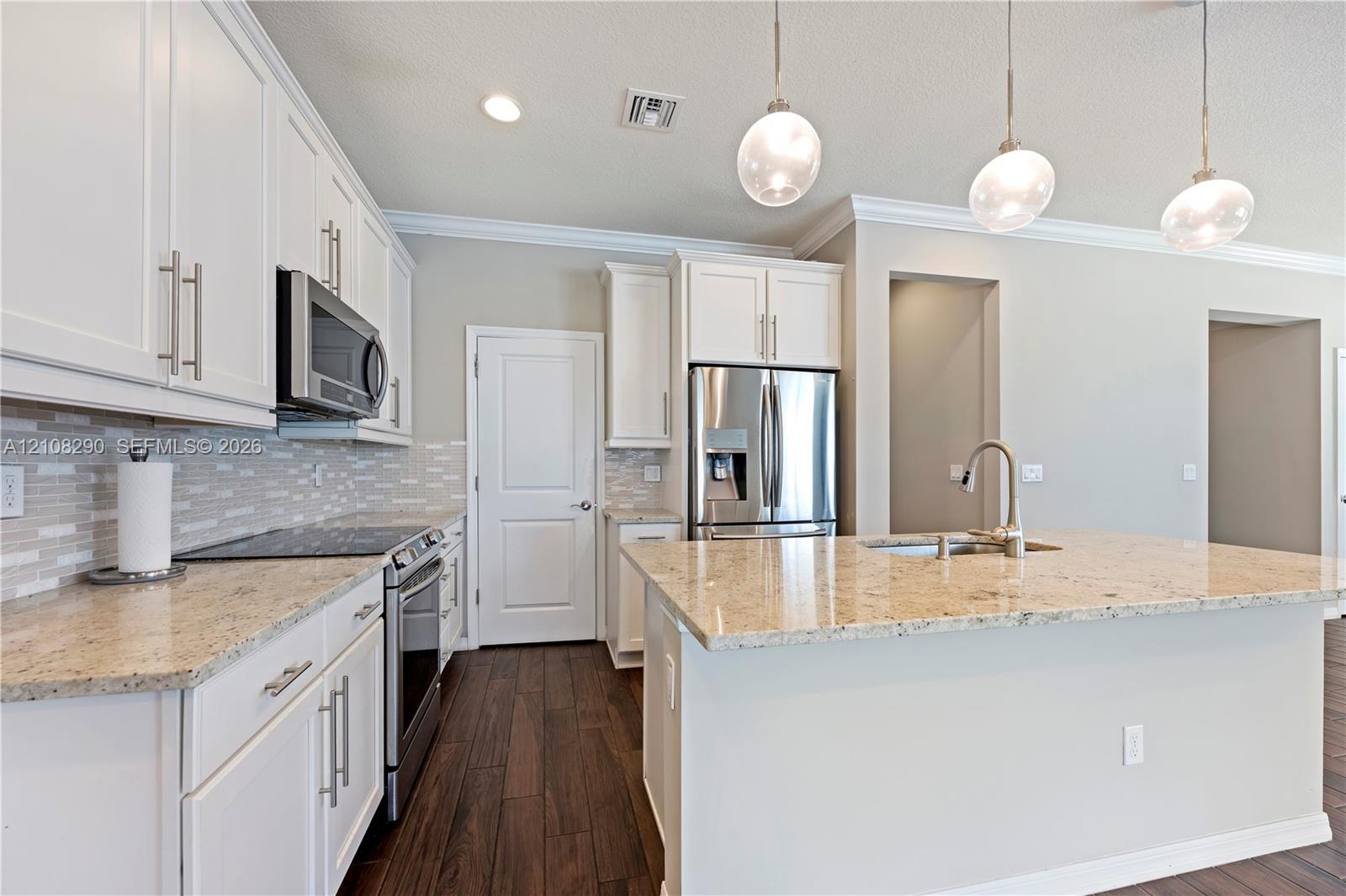 Kitchen featuring white shaker-style cabinetry, stone countertops, stainless steel appliances, decorative glass pendant lighting, and wood-finish flooring Kitchen featuring white shaker-style cabinetry, stone countertops, stainless steel appliances, decorative glass pendant lighting, and wood-finish flooring