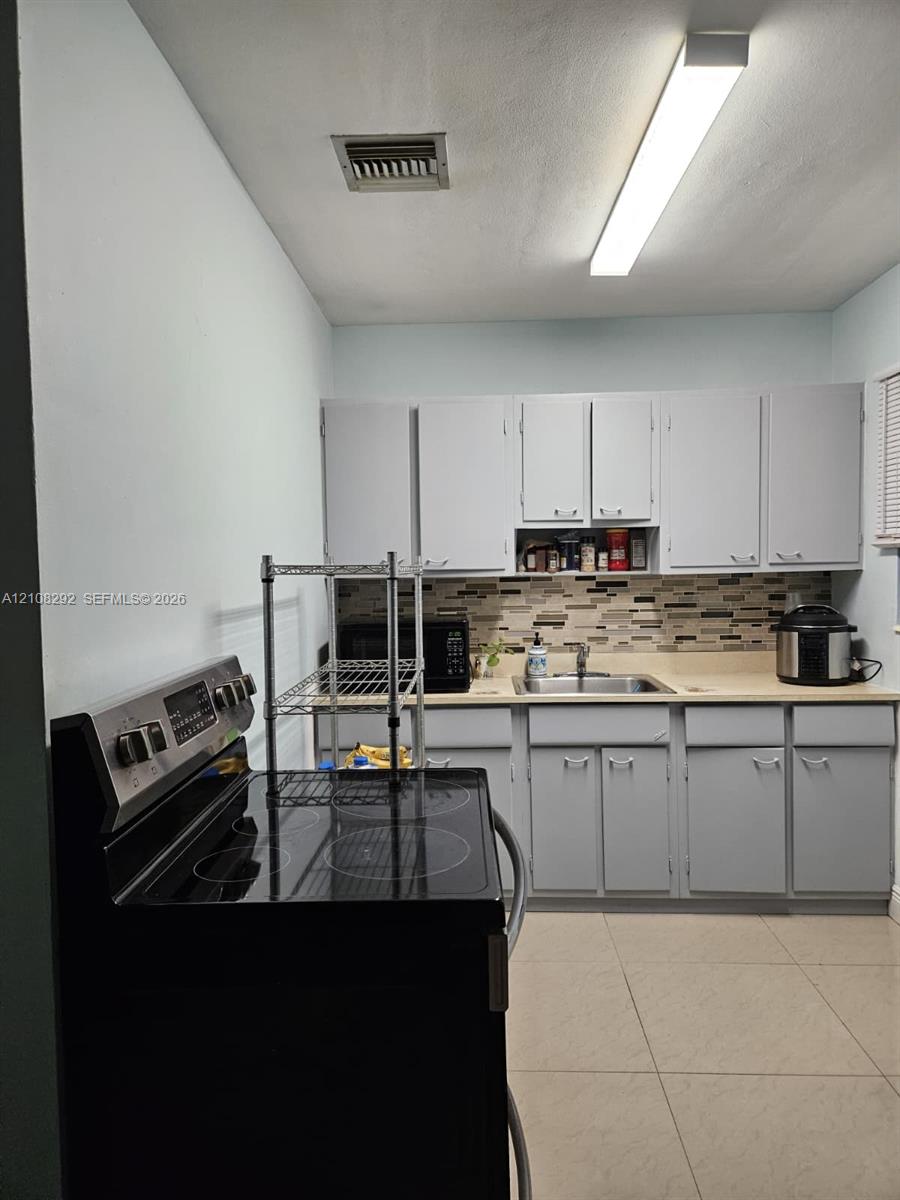 Kitchen featuring gray cabinetry, a multi-tone tile backsplash, a stainless steel sink with a mounted faucet, and large-format floor tiling