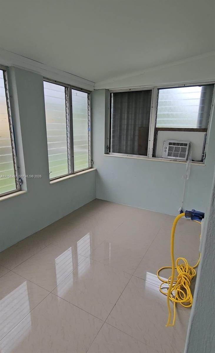 Enclosed space featuring large format light-toned tile flooring, light-colored wall paint, and multiple louvered windows