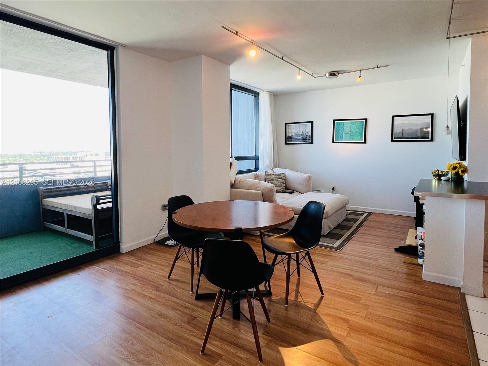 Open-concept living space featuring wood-finish flooring, floor-to-ceiling windows, attached track lighting, and a private balcony