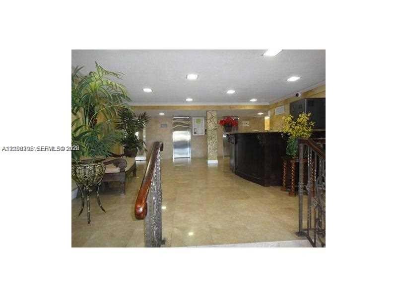Lobby featuring polished stone tile flooring, recessed ceiling lighting, a dark-toned service desk, metal elevator doors, and a wrought iron stair railing