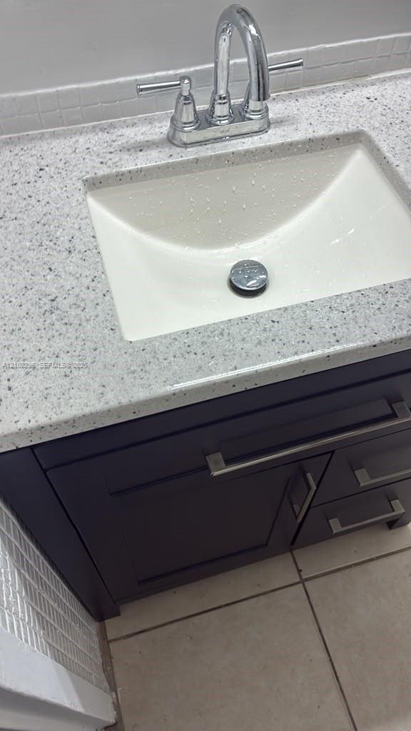 Dark-toned vanity cabinet featuring metallic bar hardware, solid-surface countertop with an integrated basin, high-arc faucet, and tiled backsplash