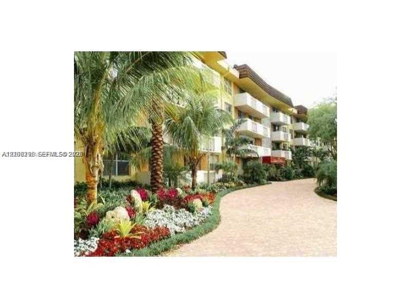 Multi-story exterior featuring private balconies, paver-style walkway, and landscaped grounds with mature palm trees and flowering foliage
