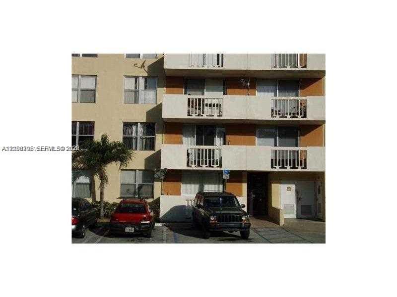 Multi-story exterior facade featuring concrete balconies with vertical railings, stucco finish, grid-pattern windows, and exterior parking