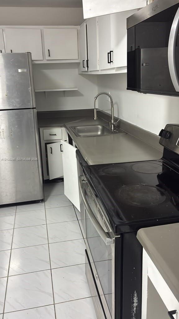 Kitchen featuring white cabinetry, stainless steel appliances, solid-surface countertops, a stainless steel sink with a high-arch faucet, and tile flooring