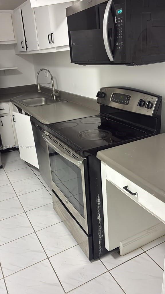 Kitchen featuring white cabinetry, stainless steel microwave, black electric range with stainless steel trim, solid-surface countertops, and tiled flooring