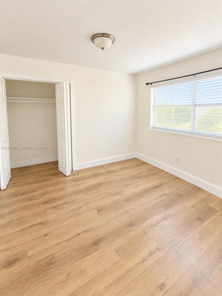 Neutral-toned interior featuring wood-finish flooring, a double-door closet, a large window with fitted blinds, and a semi-flush mount ceiling light