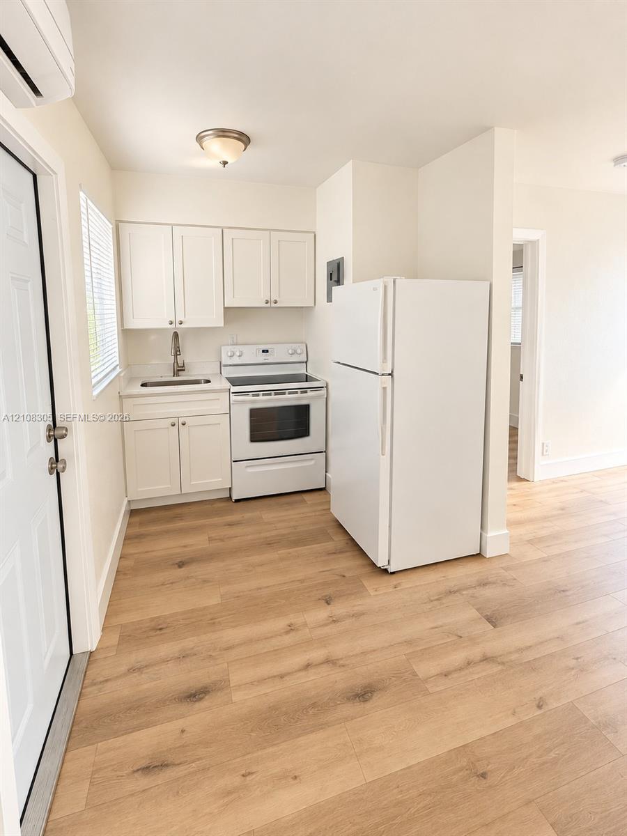 Kitchen featuring white cabinetry, wood-finish flooring, a white electric range, and a drop-in sink