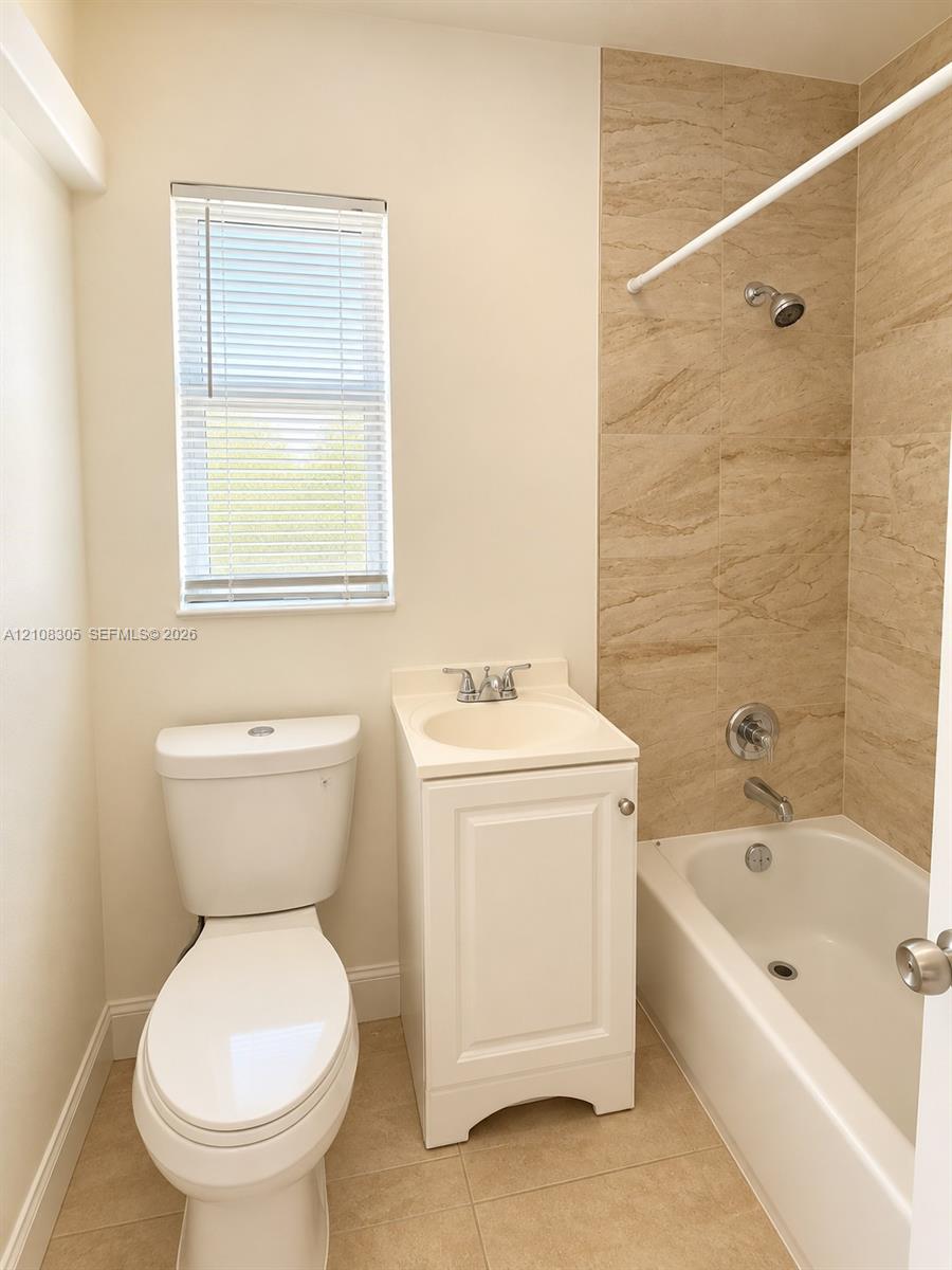 Full bathroom featuring a white pedestal vanity, tub-shower combination with natural-tone tile surround, and neutral floor tiling