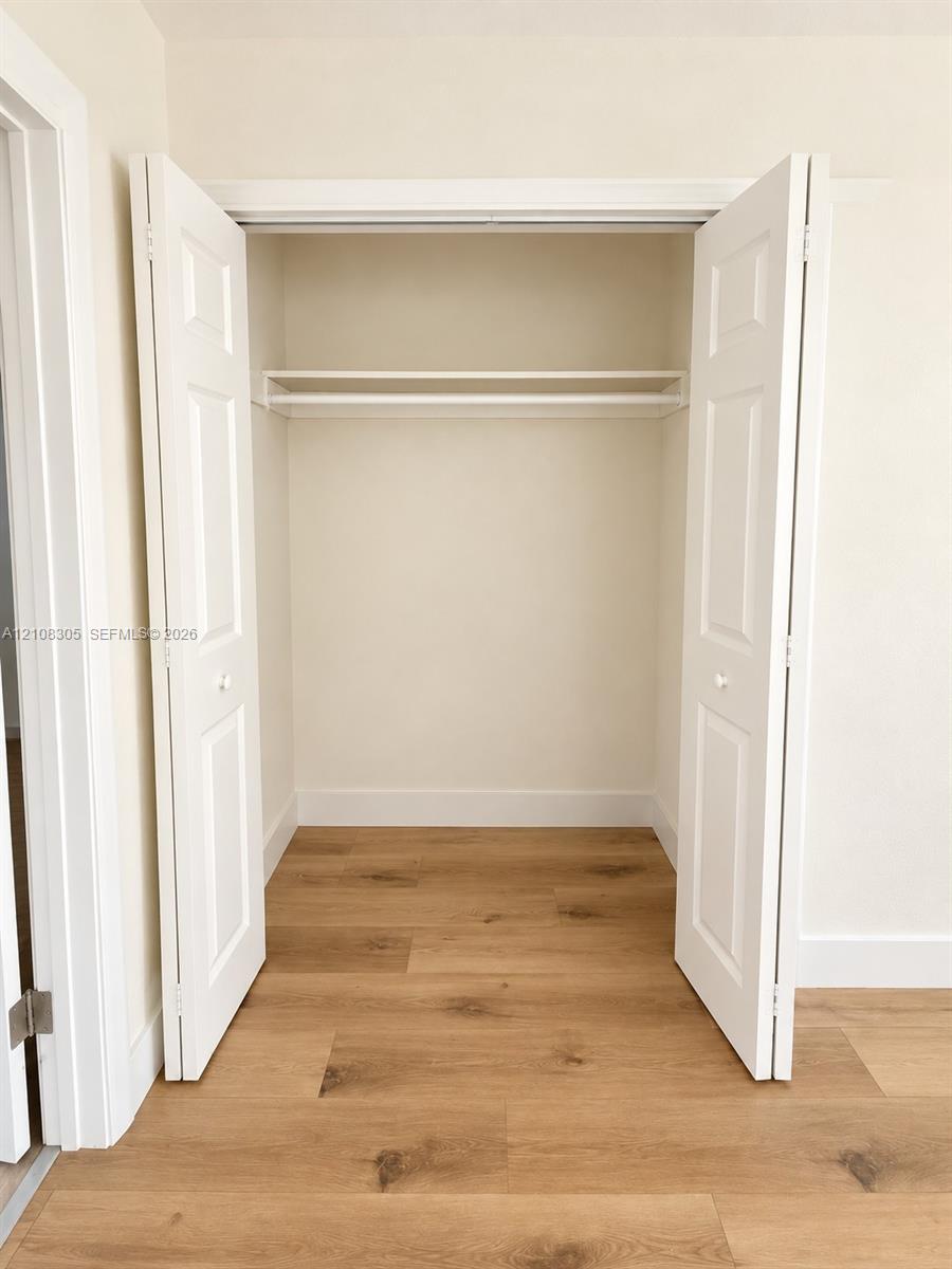 Reach-in closet featuring white bifold doors, integrated shelving, and wood-finish flooring