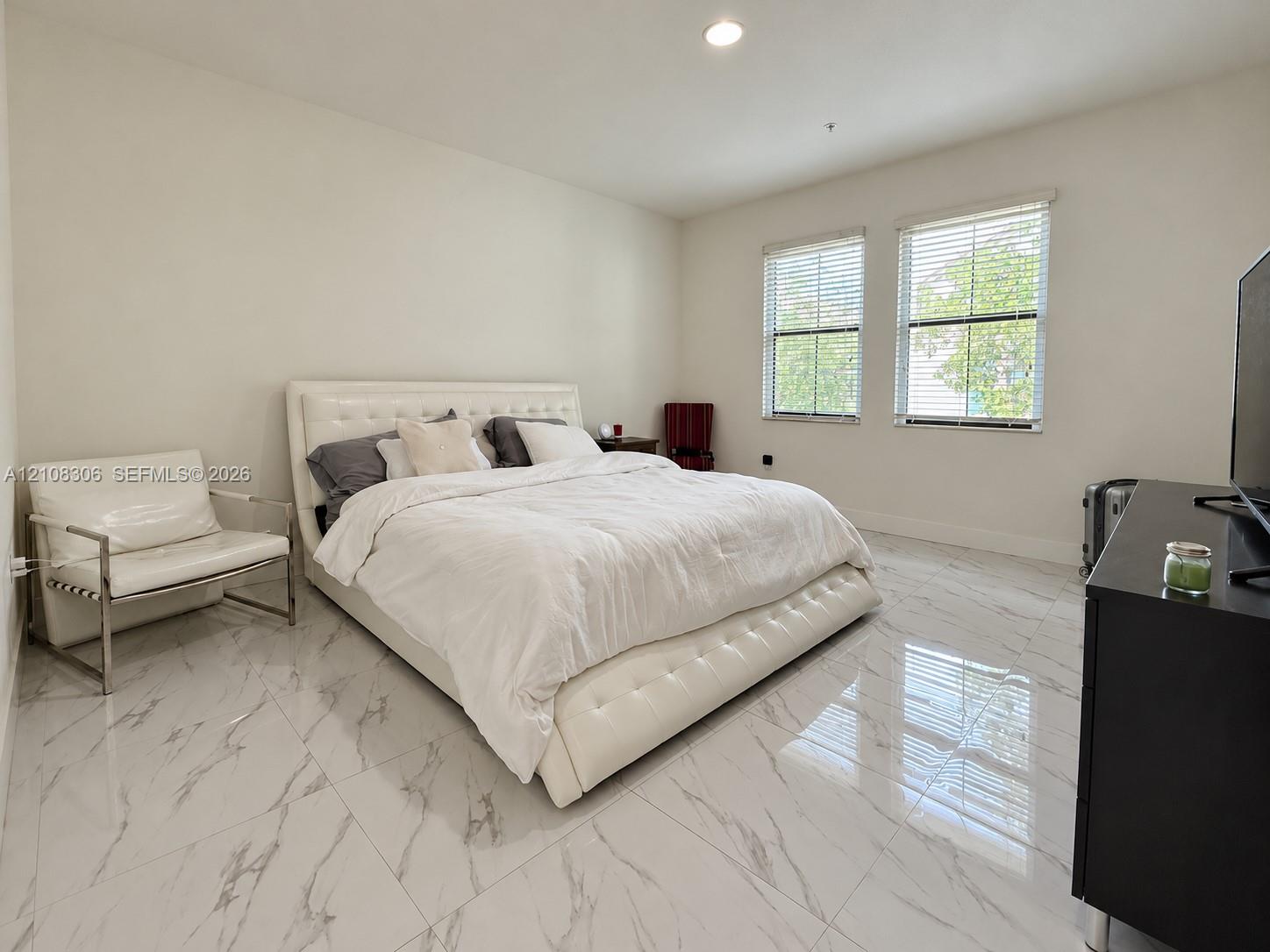 Large-format, polished stone-finish flooring with prominent veining, recessed ceiling lighting, and dual windows with horizontal blinds