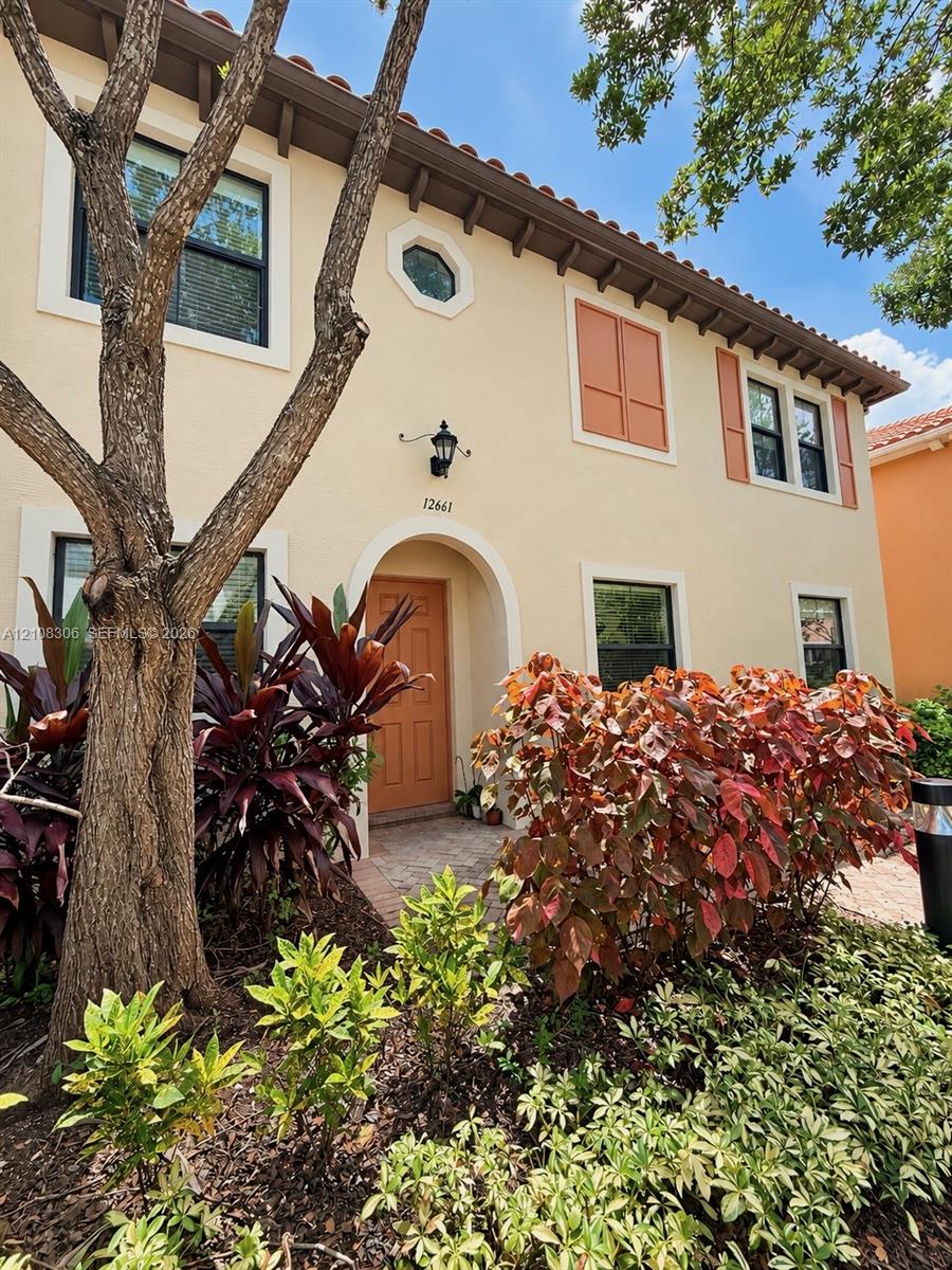 Stucco exterior featuring an arched entryway, terracotta-style roof tiles, decorative window shutters, and an octagonal accent window