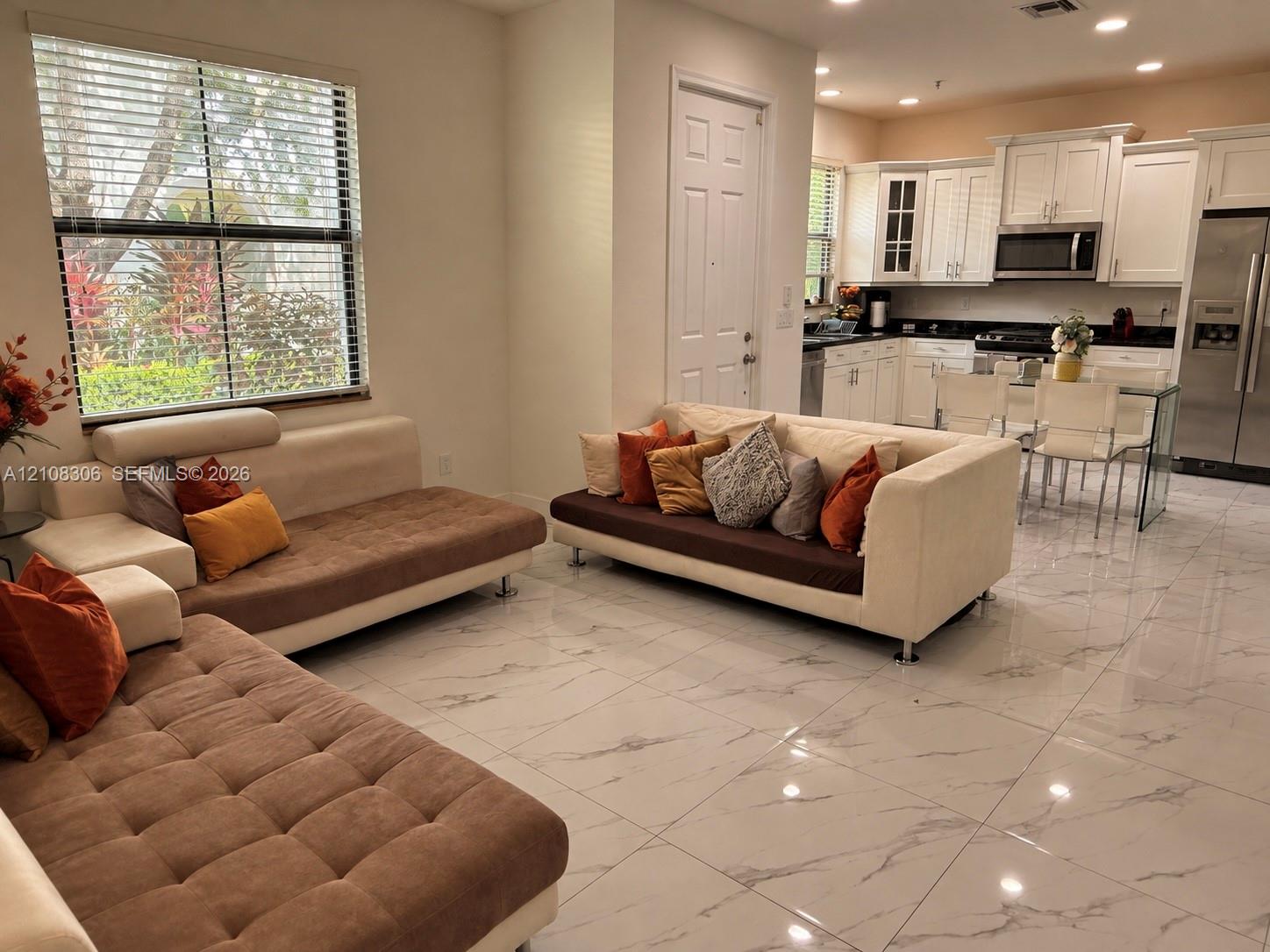 Large-format polished tile flooring, white shaker-style cabinetry, dark countertops, stainless steel appliances, and recessed lighting