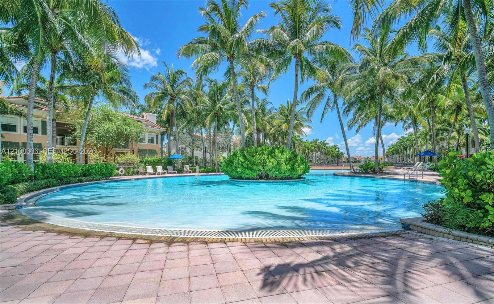 Swimming pool featuring a central landscape island, surrounded by a paved deck and mature palm trees