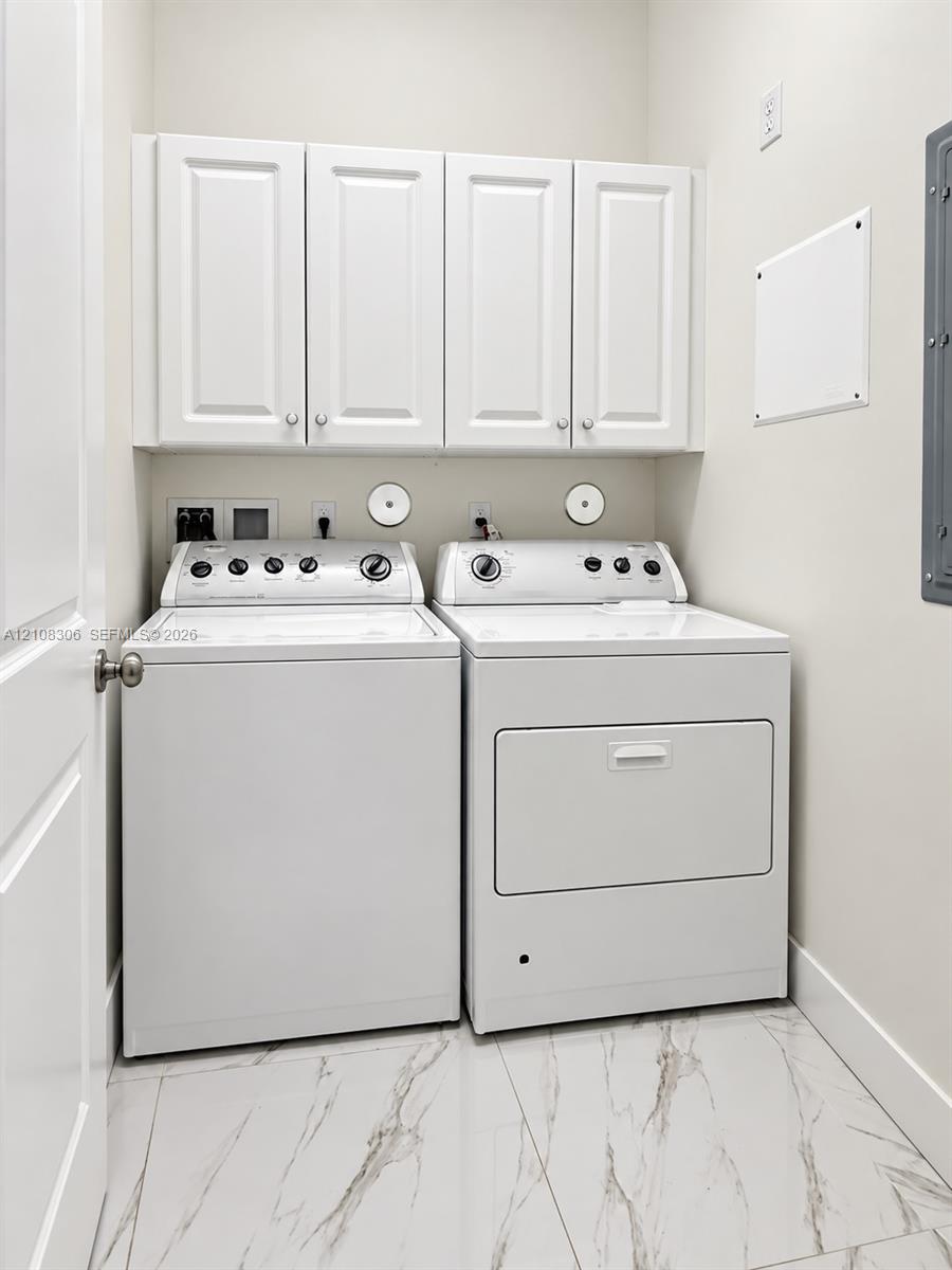 Laundry area featuring white shaker-style wall cabinets, large-format tile flooring with a veined pattern, and dedicated appliance hookups