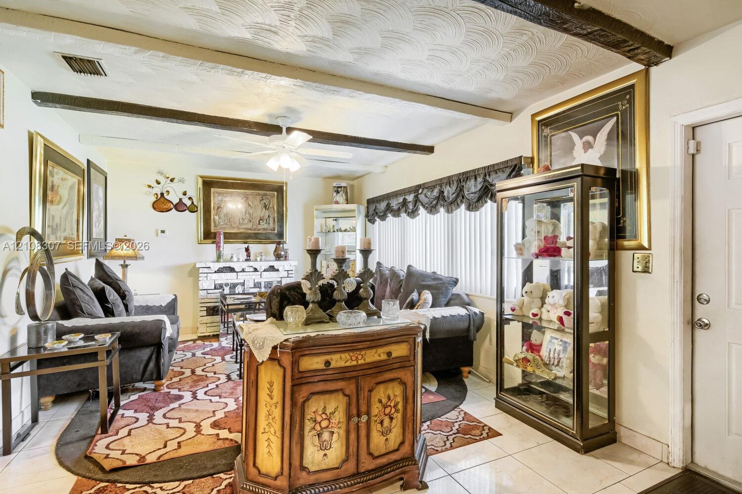 Living area featuring exposed ceiling beams, textured ceiling finish, ceramic tile flooring, built-in masonry fireplace, and ceiling fan Living area featuring exposed ceiling beams, textured ceiling finish, ceramic tile flooring, built-in masonry fireplace, and ceiling fan