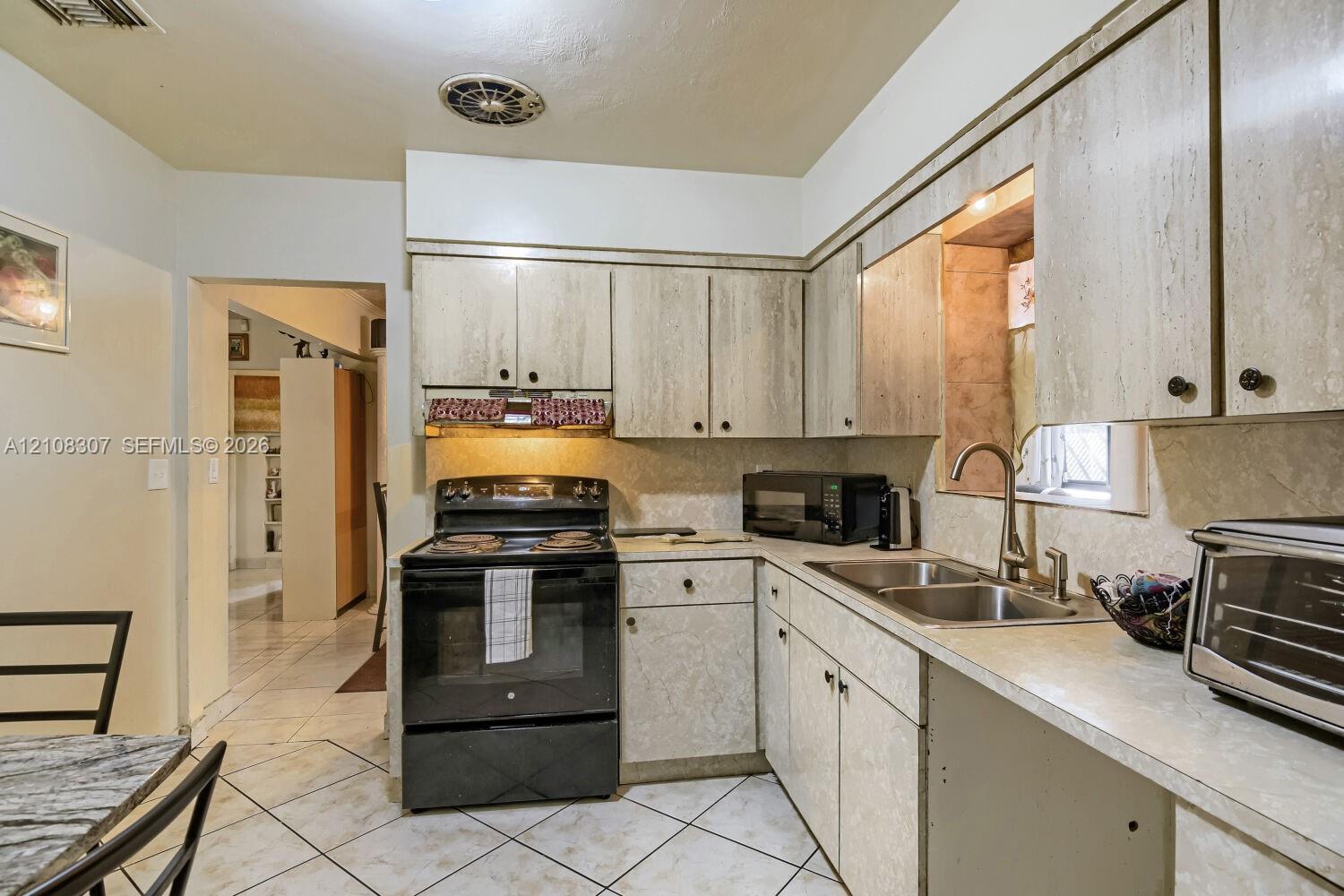 Kitchen featuring cabinetry with a stone-finish facade, stainless steel dual-basin sink, high-arc faucet, and tiled flooring Kitchen featuring cabinetry with a stone-finish facade, stainless steel dual-basin sink, high-arc faucet, and tiled flooring