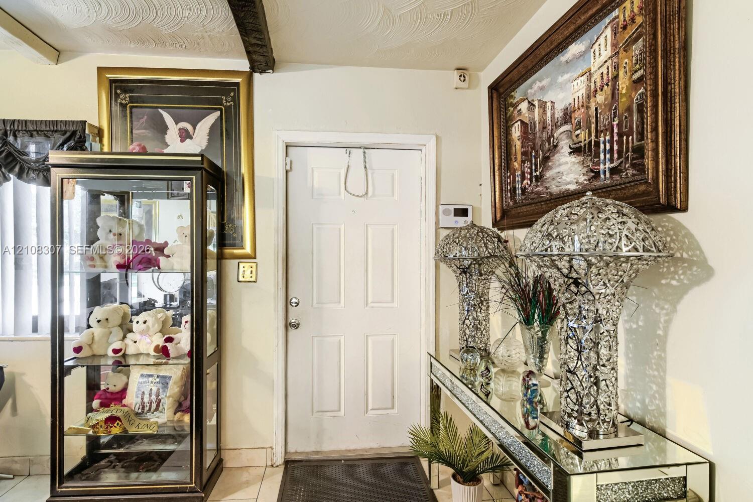 Entryway featuring a four-panel door with metallic hardware, textured ceiling, and light-colored tile flooring Entryway featuring a four-panel door with metallic hardware, textured ceiling, and light-colored tile flooring
