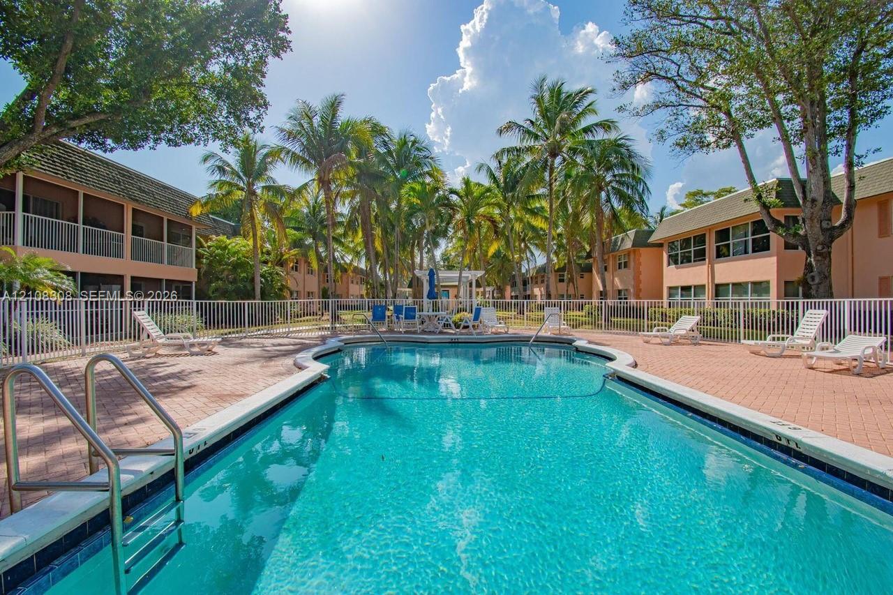 Swimming pool with a paved deck, metal perimeter fencing, and mature palm trees