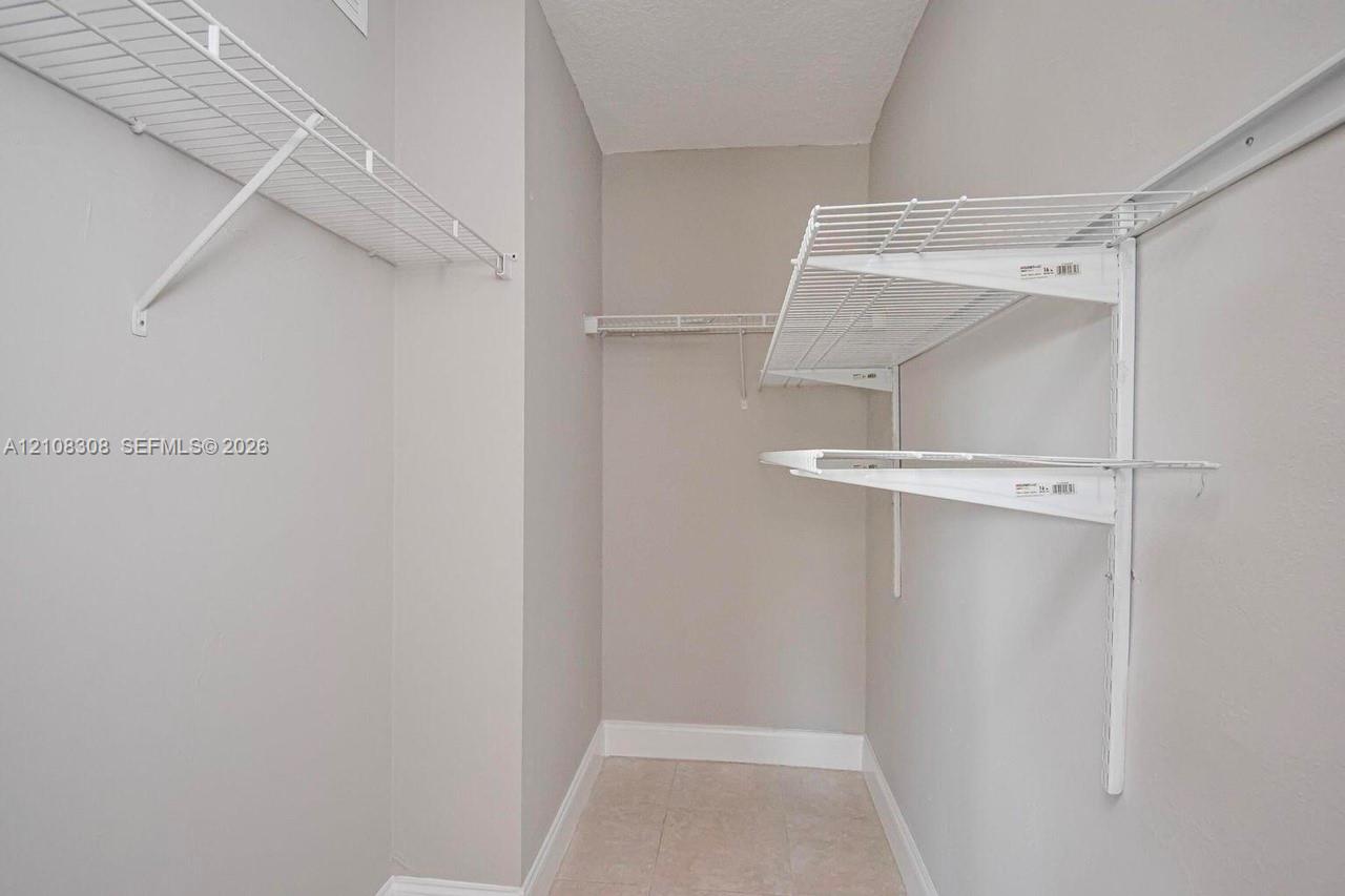 Walk-in storage space featuring neutral wall paint, tile flooring, and white wire shelving systems