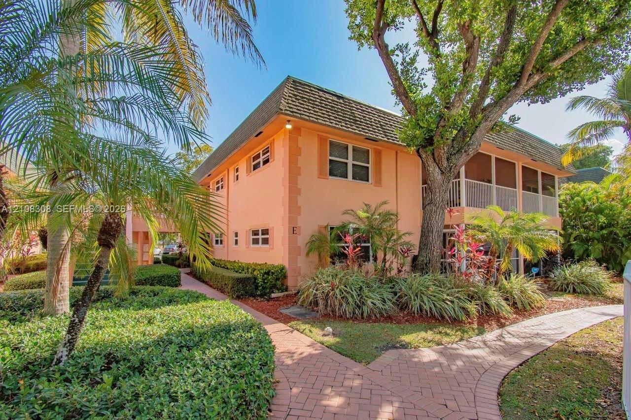 Two-story stucco exterior with a hip roof, multi-level screened-in balconies, paver walkways, and mature tropical landscaping