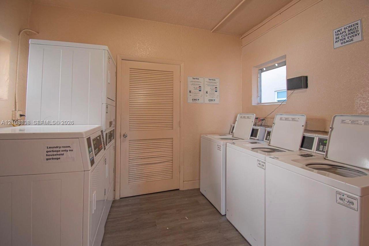 Laundry facility featuring multiple top-load washers, a stackable dryer unit, louvered interior door, and wood-finish flooring