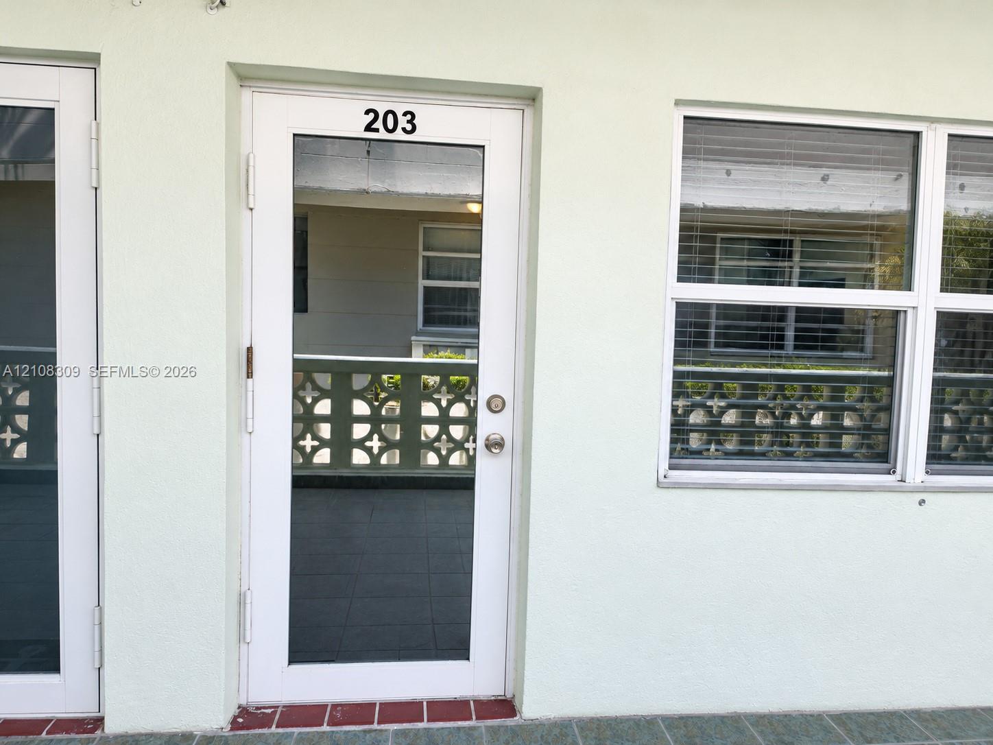 White-framed glass entry door, multi-pane window with integrated blinds, and decorative concrete screen wall