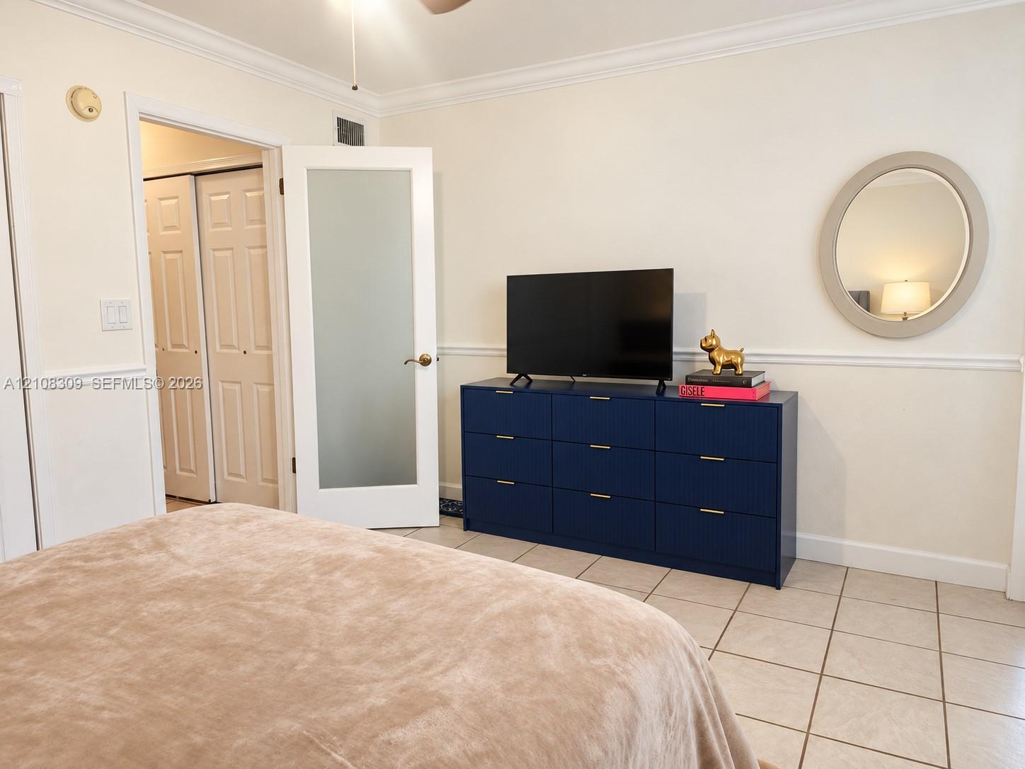 Room featuring neutral wall-to-wall ceramic tile flooring, crown molding, chair rail trim, and a frosted glass-panel interior door