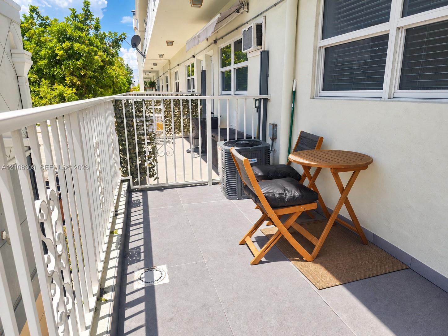Covered balcony featuring large-format gray tile flooring, white metal railing, and wall-mounted exterior lighting