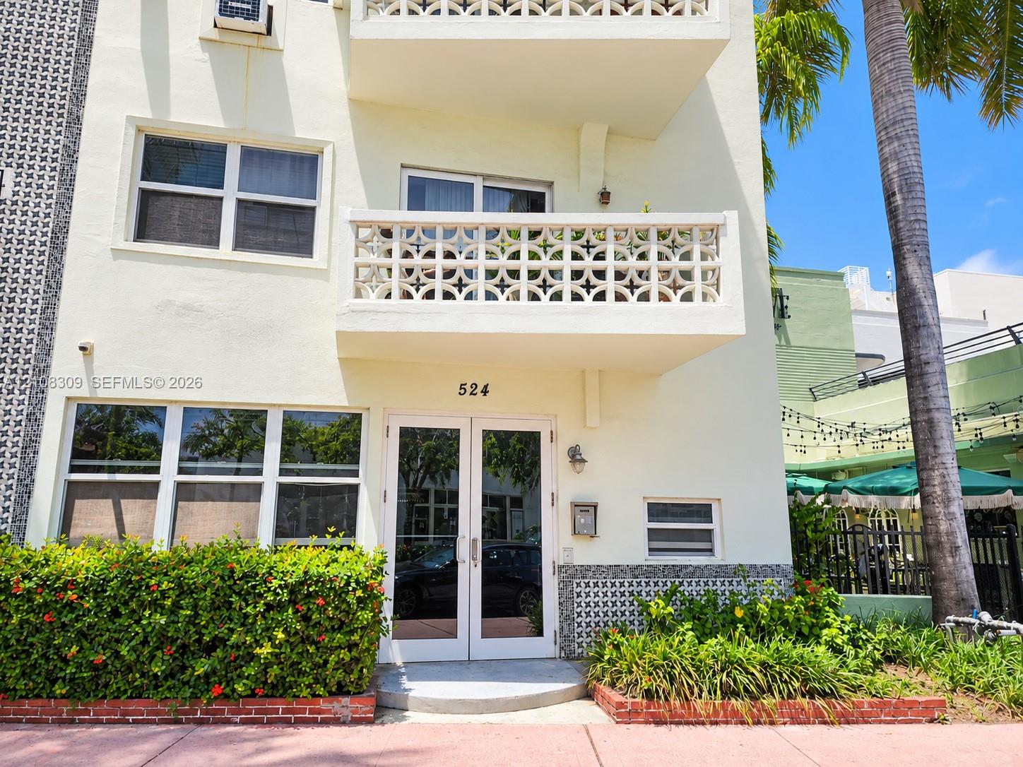 Exterior facade featuring decorative concrete masonry screen walls, private balcony, glass-paneled double entry door, and manicured landscaping with brick edging Exterior facade featuring decorative concrete masonry screen walls, private balcony, glass-paneled double entry door, and manicured landscaping with brick edging