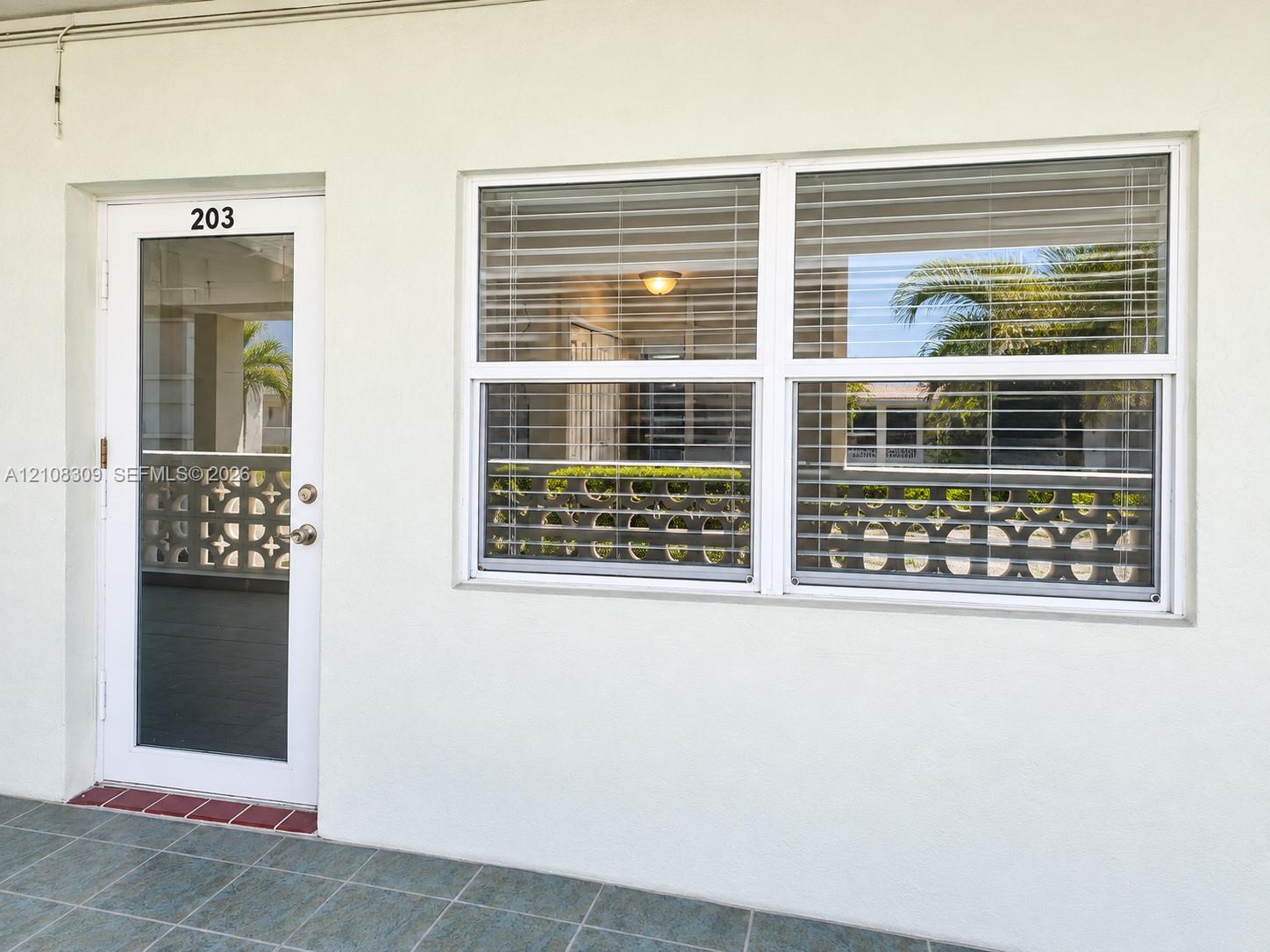Exterior entrance featuring a white-framed glass entry door, a multi-pane horizontal window with integrated blinds, and tile flooring