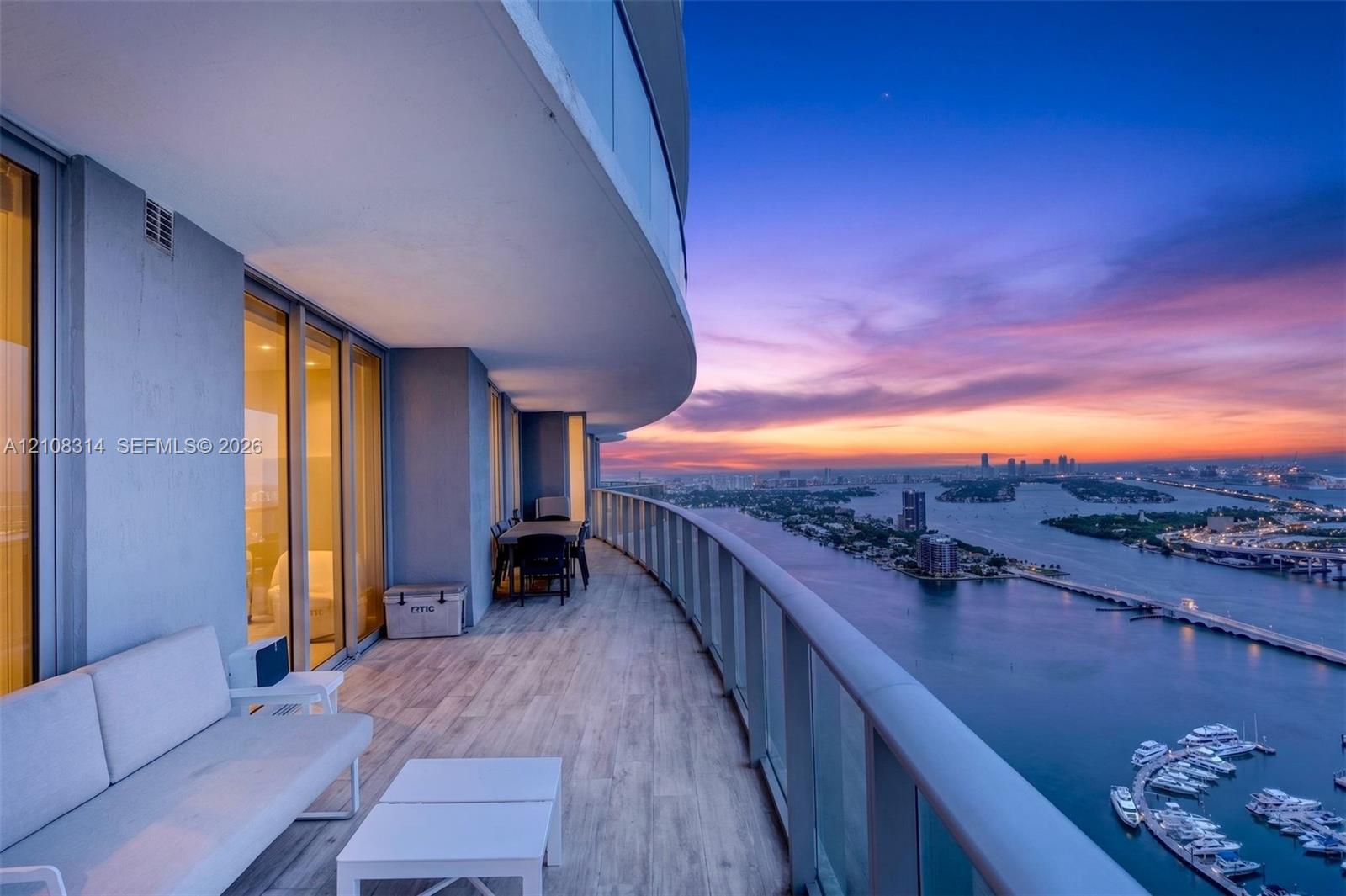 Expansive covered balcony featuring tile flooring, glass panel railings, and floor-to-ceiling glass wall panels