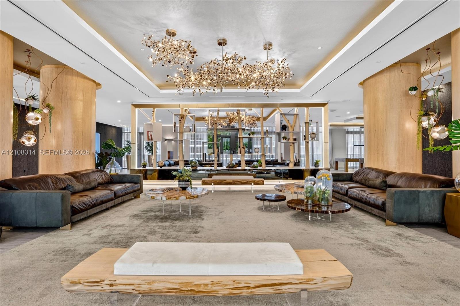 Expansive room featuring cylindrical wood-finished support columns, custom multi-cluster decorative chandeliers, recessed tray ceiling lighting, and a floor-to-ceiling built-in geometric wood-frame partition