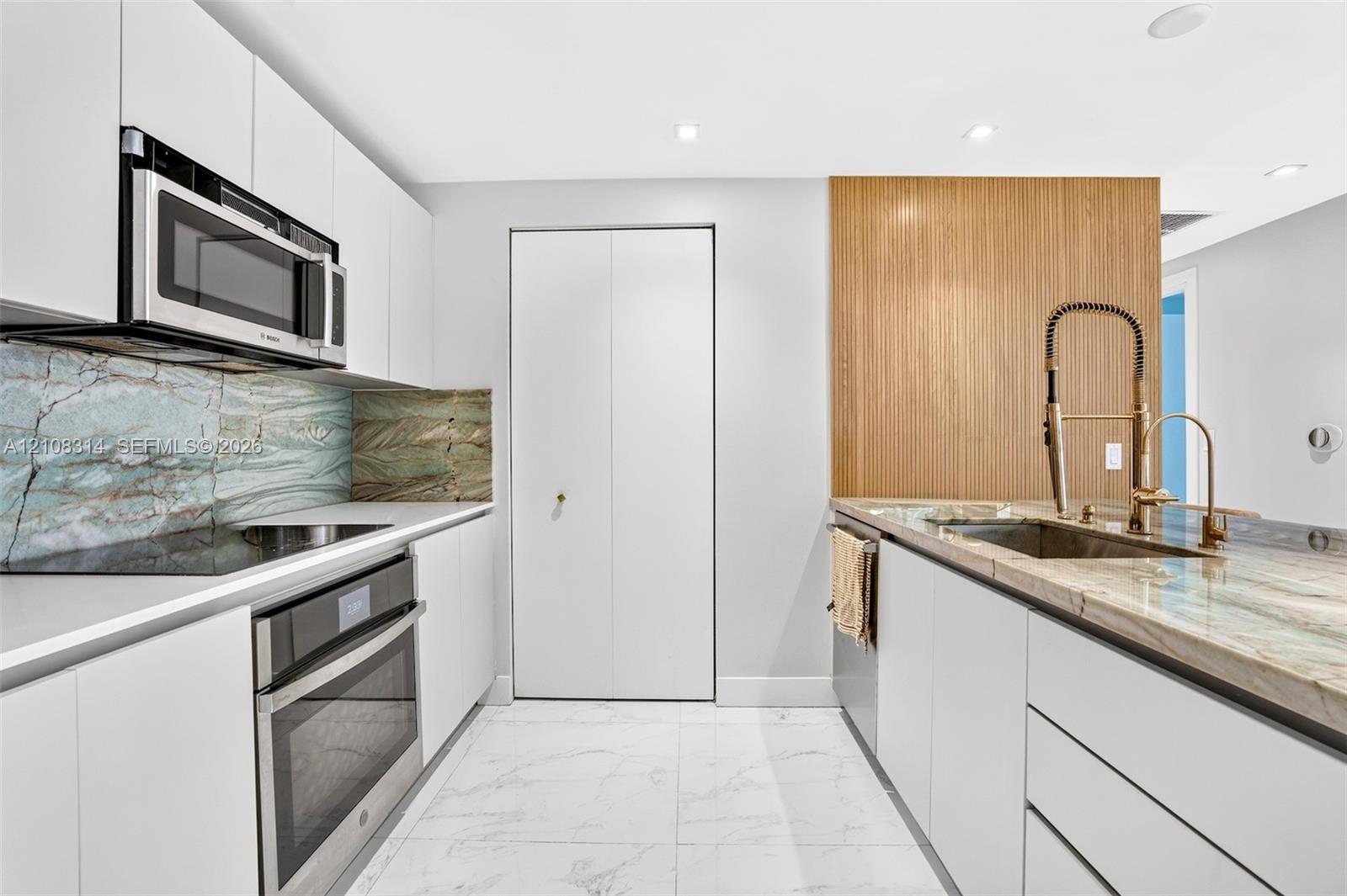 Modern kitchen featuring flat-panel white cabinetry, stone slab countertops, integrated stainless steel appliances, and wood-finish accent paneling with a gooseneck faucet Modern kitchen featuring flat-panel white cabinetry, stone slab countertops, integrated stainless steel appliances, and wood-finish accent paneling with a gooseneck faucet