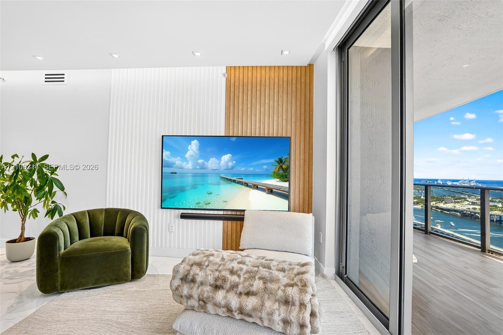 Custom accent wall featuring vertical wood-slat and fluted detailing, recessed ceiling lighting, and expansive floor-to-ceiling sliding glass doors leading to a private balcony