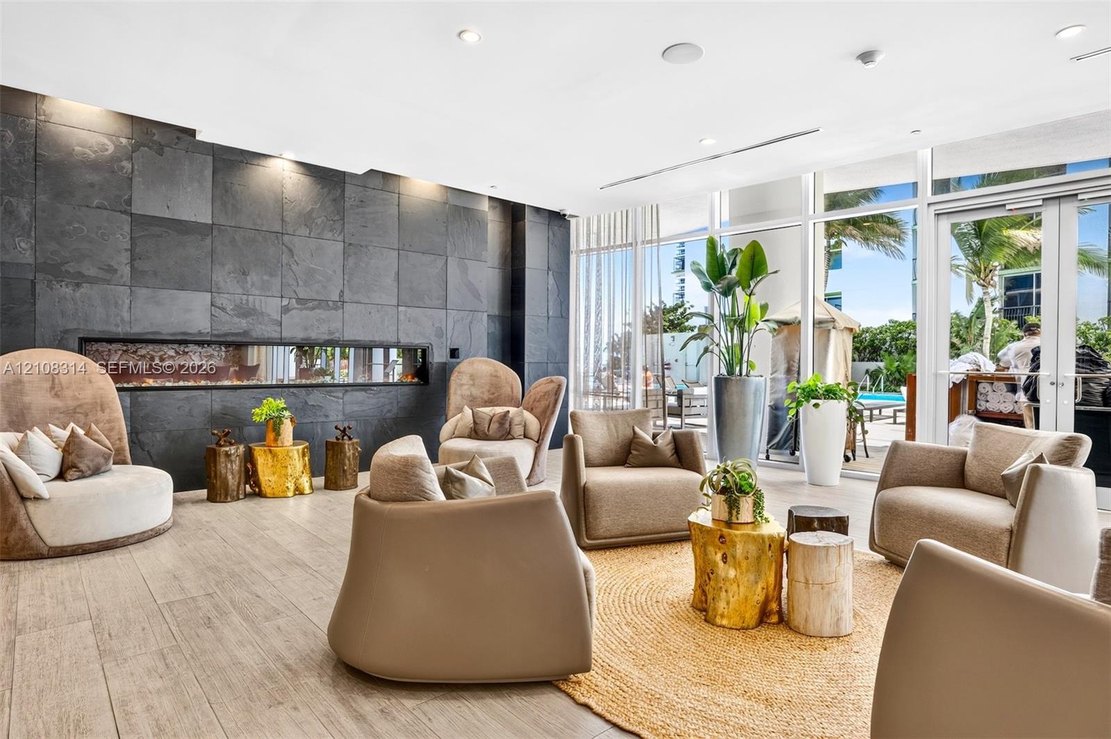 Large-format stone tile accent wall featuring a built-in linear fireplace, wood-finish flooring, and floor-to-ceiling glass paneling