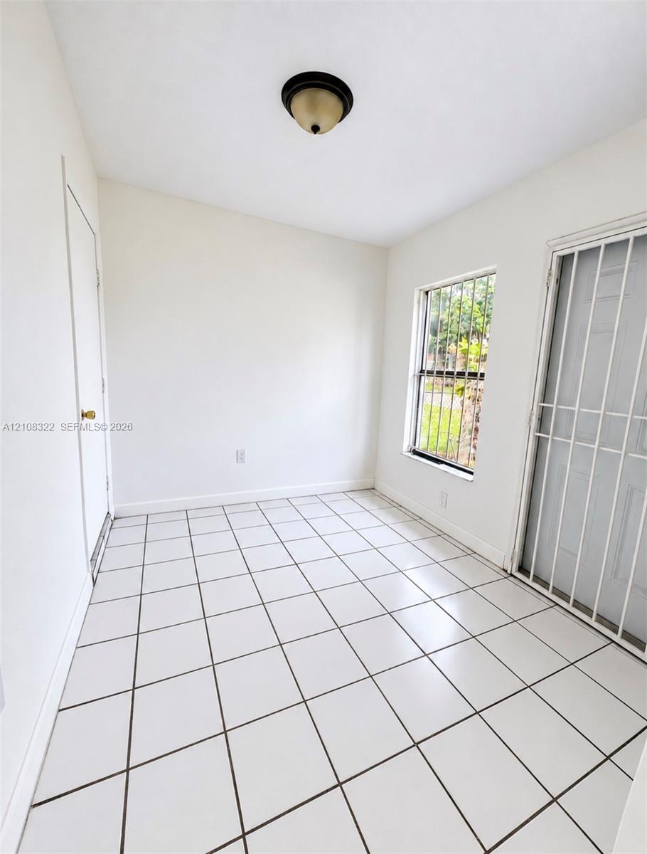 Interior space featuring white tile flooring, flush-mount ceiling lighting, and a metal security door Interior space featuring white tile flooring, flush-mount ceiling lighting, and a metal security door