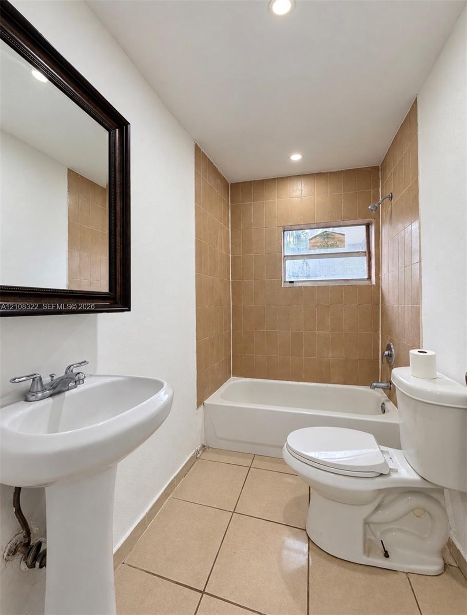 Bathroom featuring a porcelain pedestal sink, ceramic tile flooring, a shower-tub combination with tiled surround, and a framed wall-mounted mirror