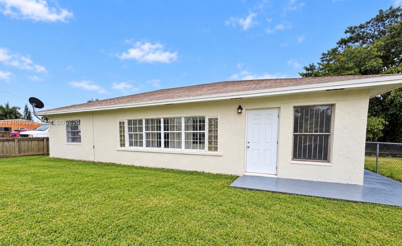 Stucco exterior featuring an expansive multi-pane window configuration, glass block accents, covered concrete patio, and mature lawn Stucco exterior featuring an expansive multi-pane window configuration, glass block accents, covered concrete patio, and mature lawn